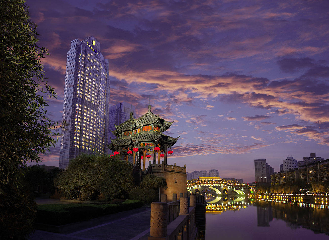Chengdu 桌布 壁紙 — 一座傳統中式亭閣掛著紅燈籠，在黃昏時分矗立河邊，在紫橙色的天空下映照著現代摩天大樓。