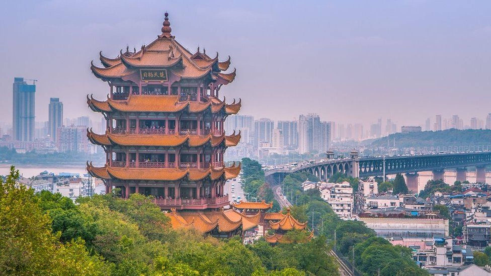 Wuhan 桌布 壁紙 — 一座傳統中式寶塔，橙色屋頂，矗立於翠綠山丘之上，俯瞰現代城市與河橋。
