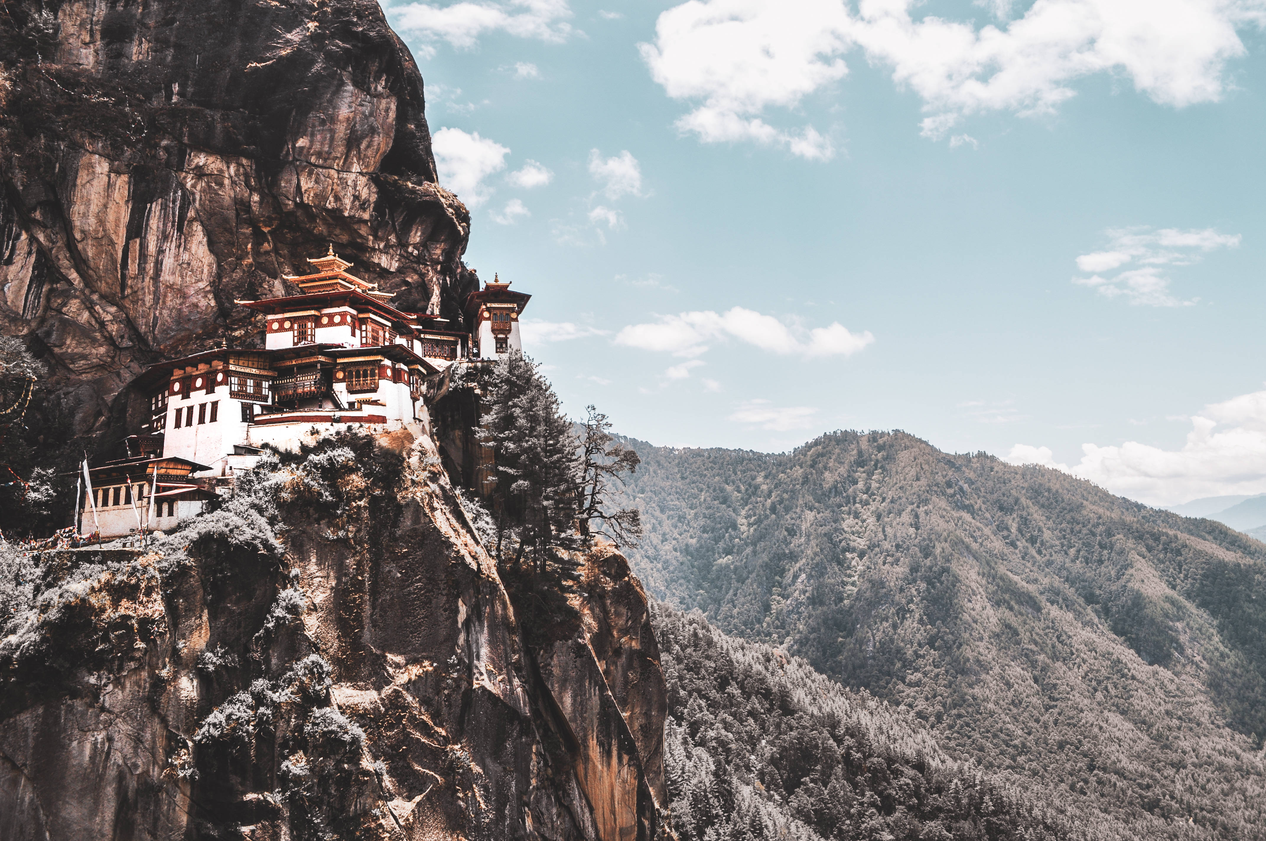 Bhutan 桌布 壁紙 — 一座傳統佛教寺院依附在白雪覆蓋的懸崖上，俯瞰著廣闊的山谷，天空湛藍明亮。