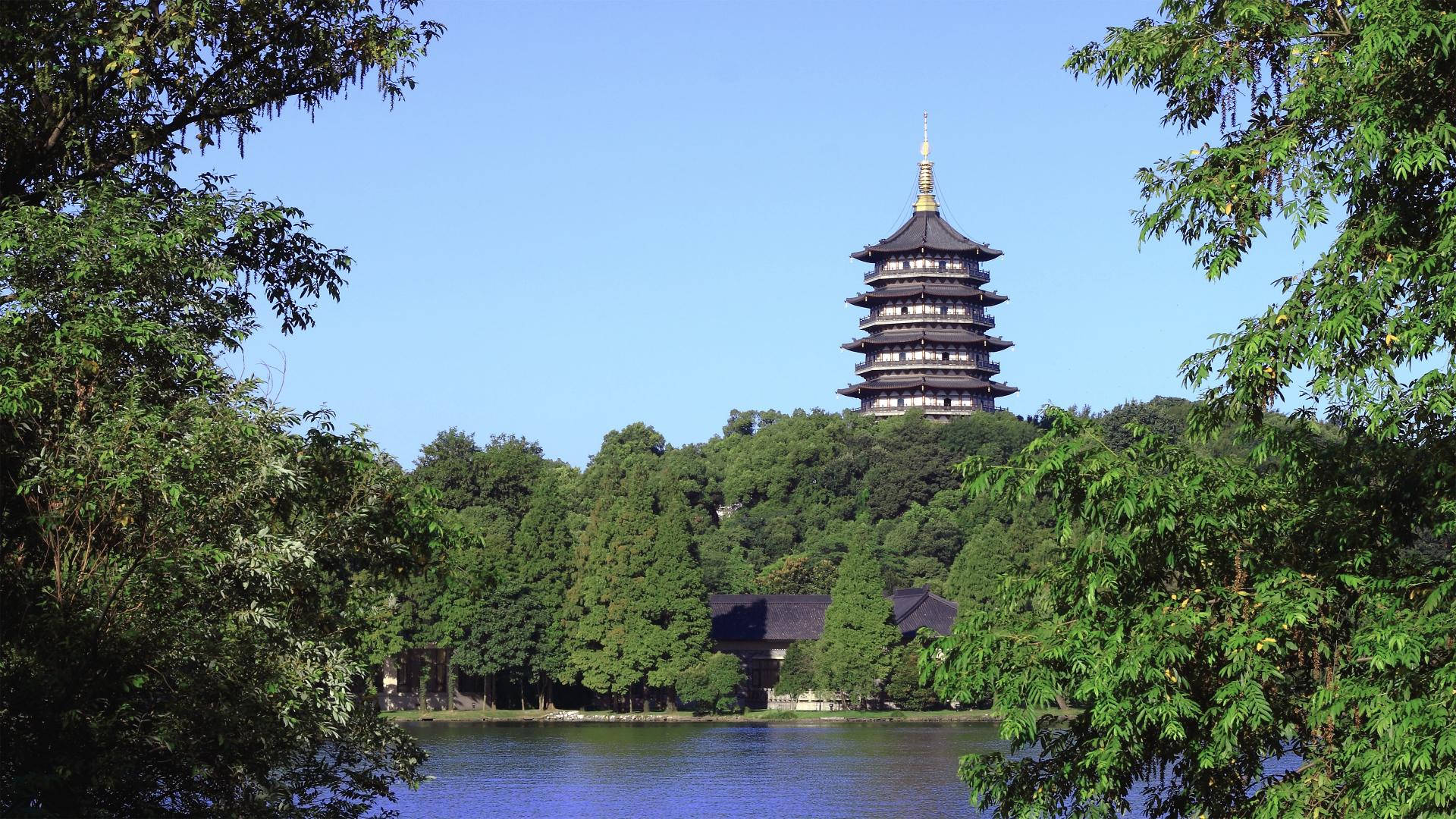 Hangzhou 桌布 壁紙 — 一座傳統多層寶塔聳立在翠綠樹木之上，旁邊是平靜的藍色湖泊，天空晴朗。