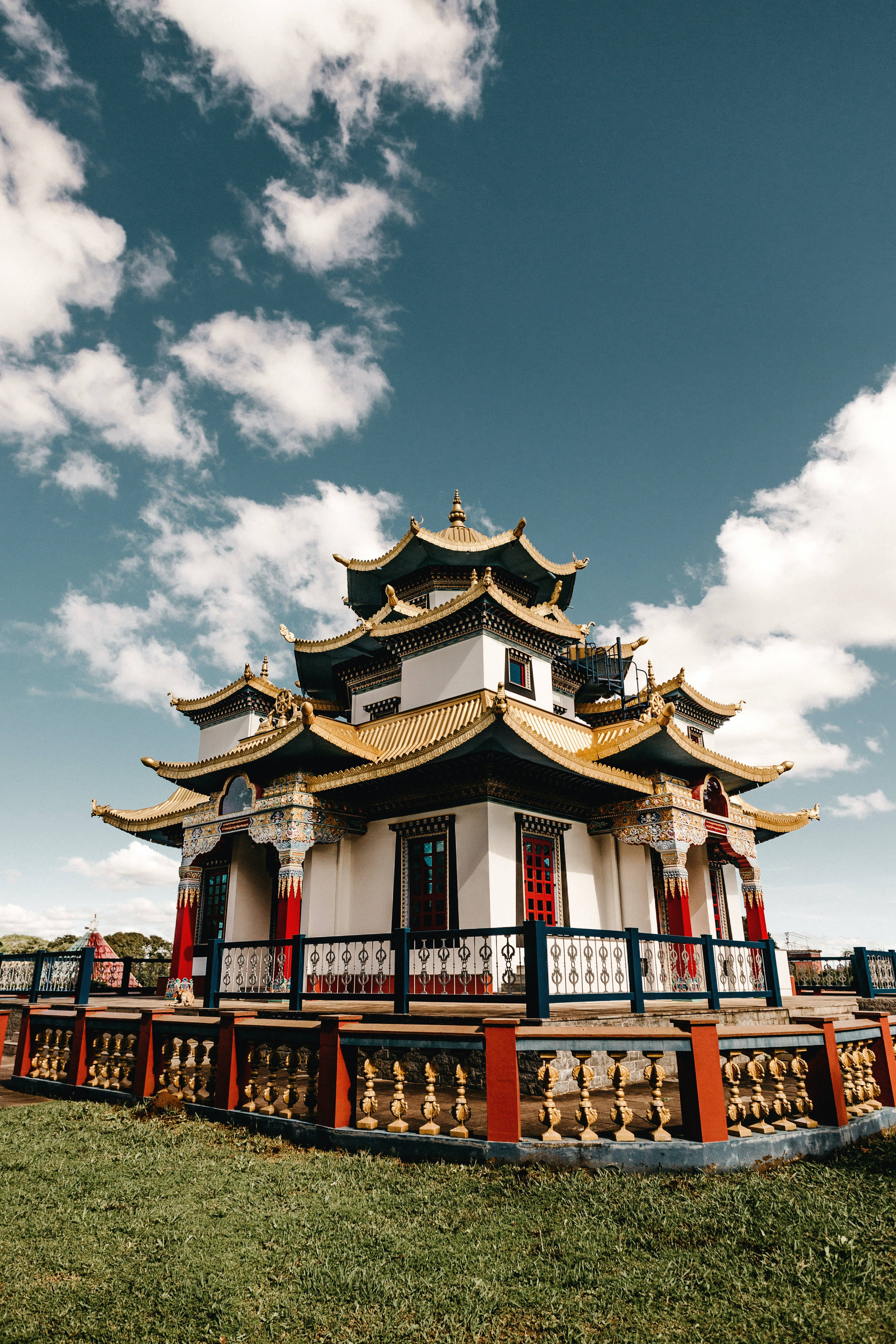 中式房屋壁紙 桌布 壁紙 — 一座傳統多層寺廟，擁有金色屋頂和紅色柱子，在點綴著蓬鬆白雲的明亮藍天下傲然矗立。
