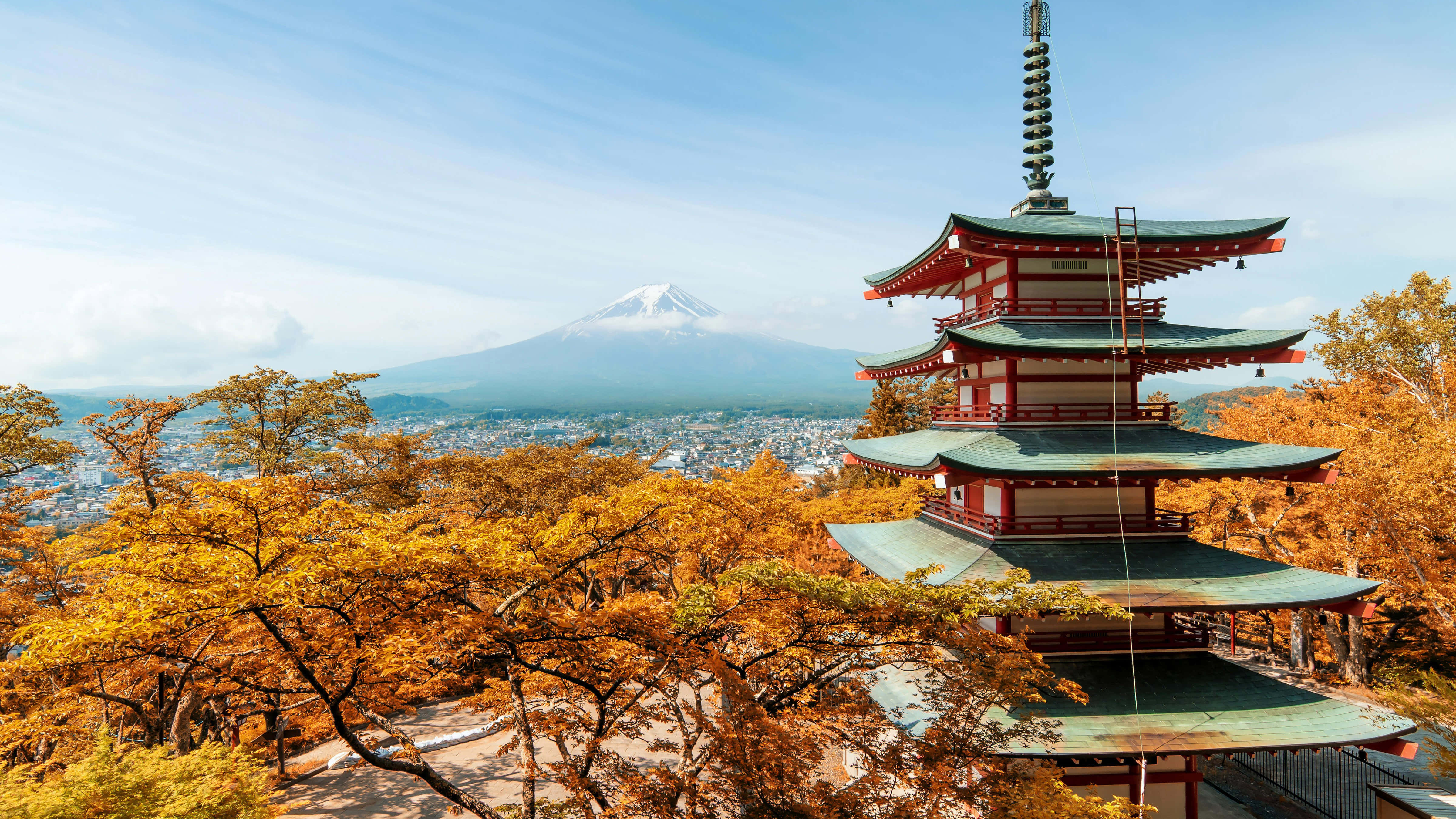 日式 桌布 壁紙 — 一座傳統日本寶塔矗立在金黃色的秋樹之中，遠處可見積雪的富士山，在清澈的藍天下。
