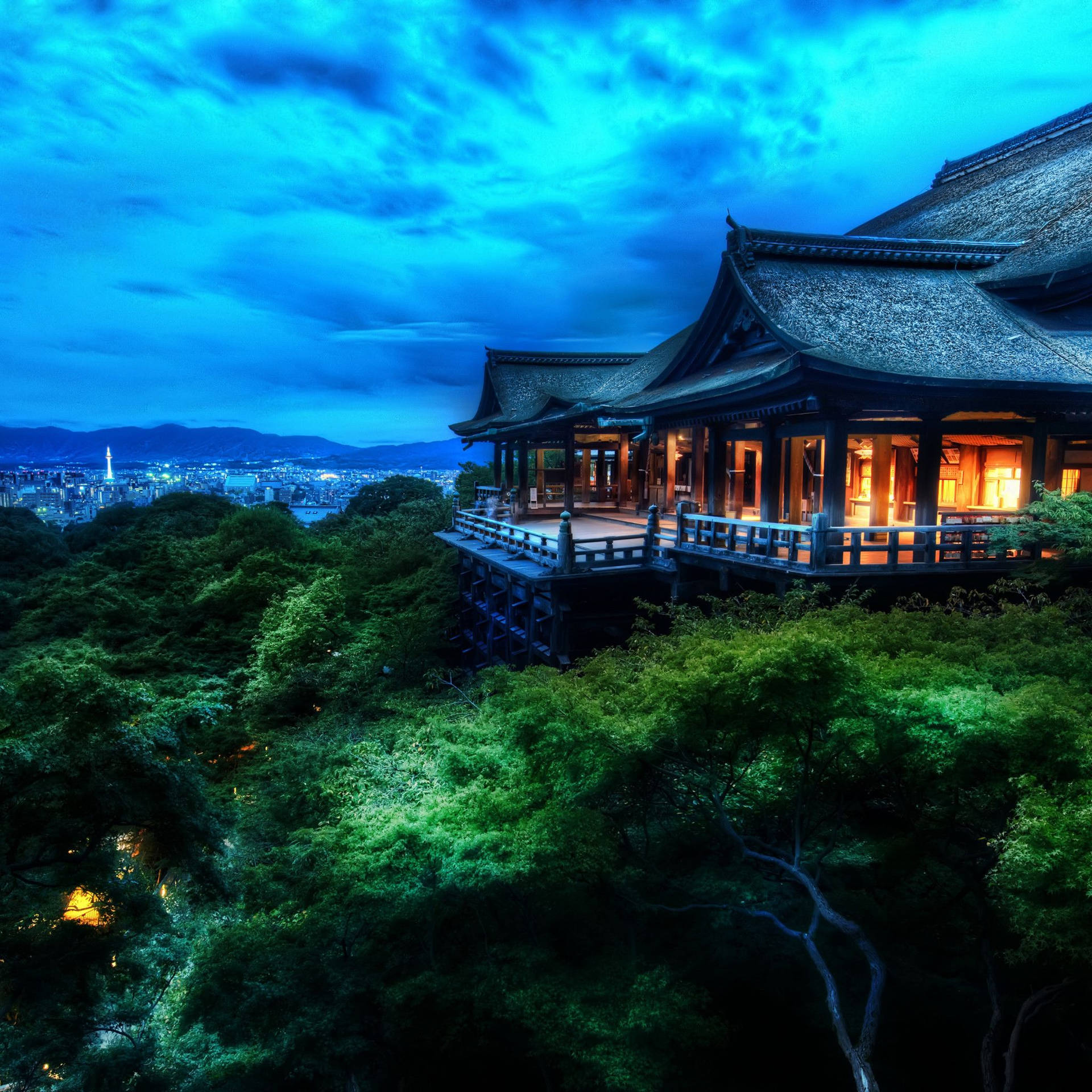 一座發光的寺廟在山上，被樹木環繞，俯瞰著黃昏時分的城市。 — iPad mini 動態圖片 壁紙