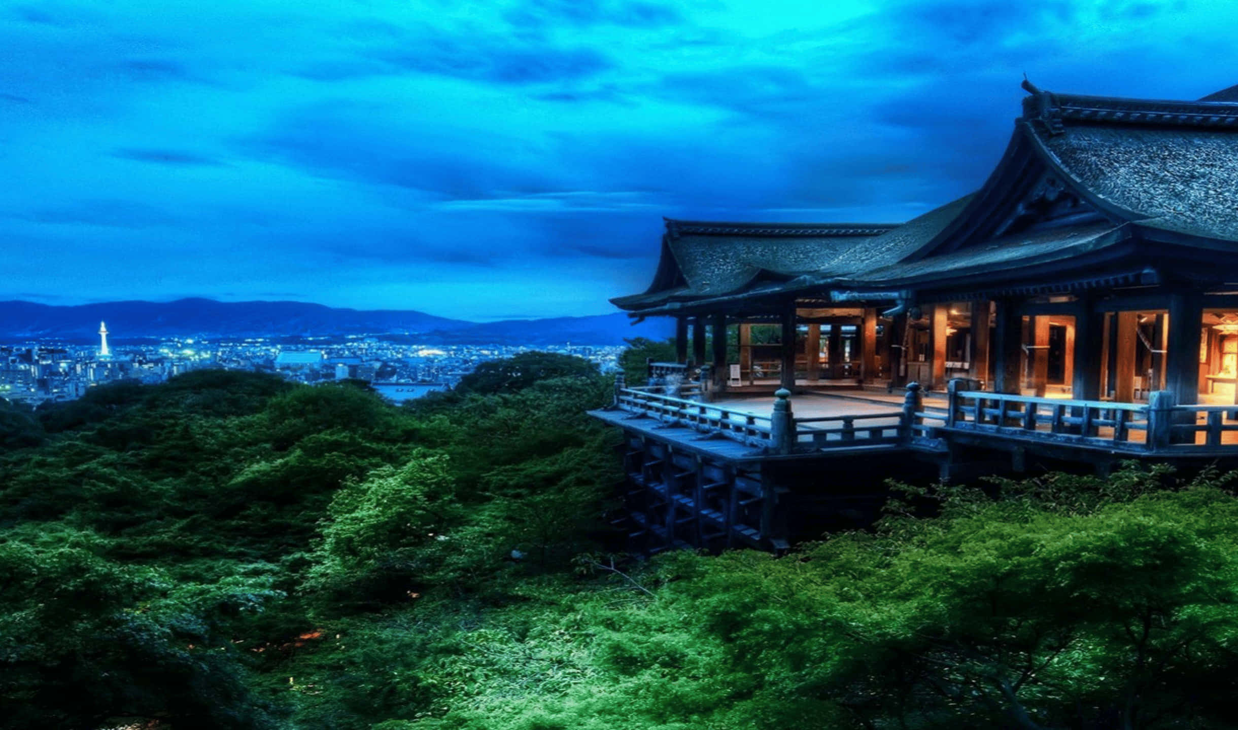 2440x1440 Monitor 桌布 壁紙 — 一座傳統木造寺廟坐落在鬱鬱蔥蔥的山丘上，俯瞰著深藍色暮色天空下的廣闊城市景觀。