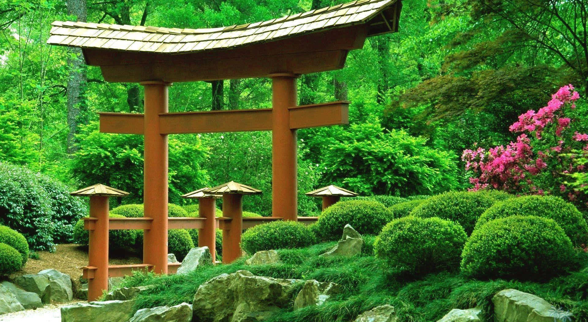 Samurai Garden 桌布 壁紙 — 一座傳統的木製鳥居矗立在鬱鬱蔥蔥的日本花園中，園內有修剪整齊的灌木、粉紅色的花朵和長滿苔蘚的石頭。