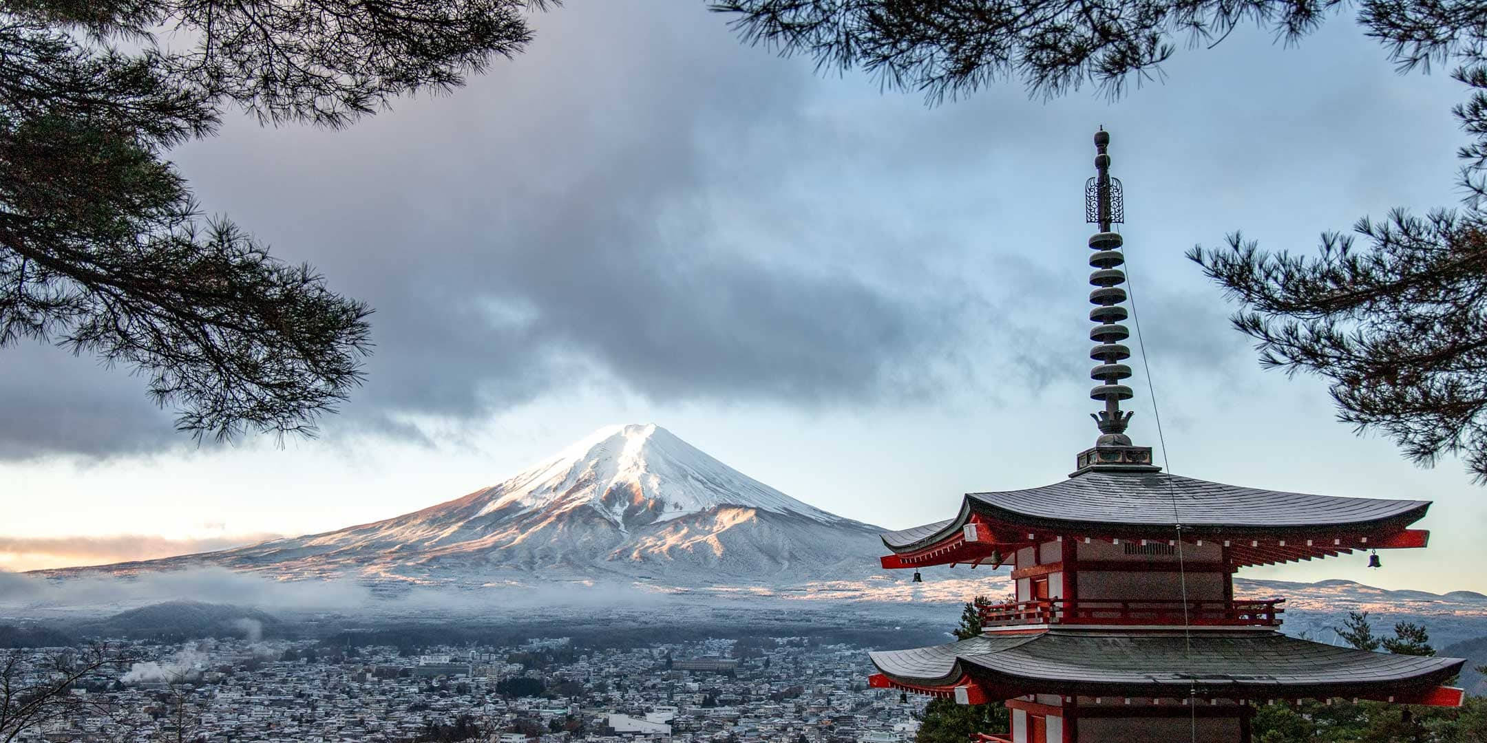 Asia 桌布 壁紙 — 一座傳統的紅色日本寶塔框住了雄偉的雪覆蓋的富士山，背景是戲劇性的多雲天空。
