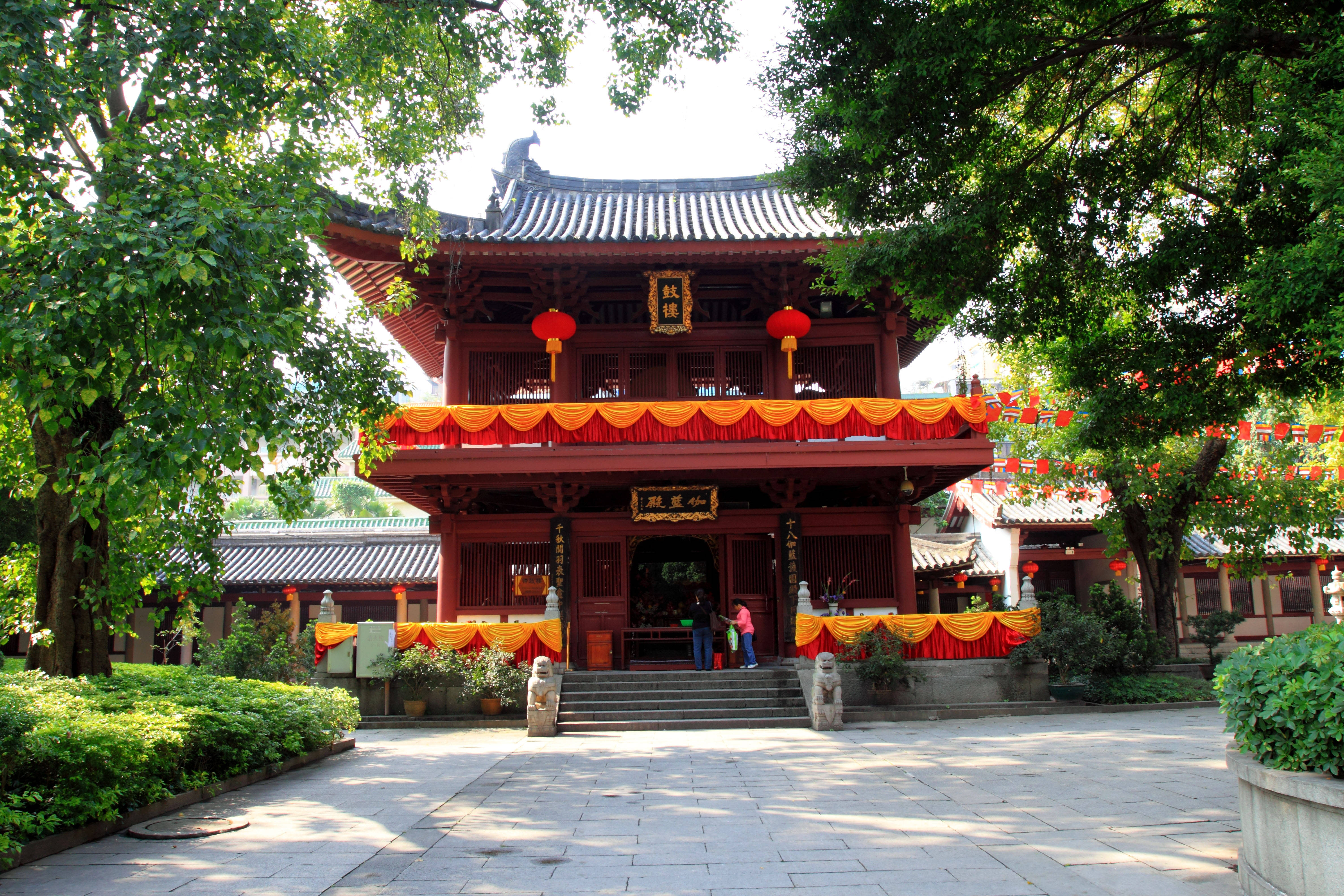 Guangzhou 桌布 壁紙 — 一座傳統的紅色木造寺廟，擁有華麗的屋頂和橙色窗簾，在晴朗的日子裡矗立在明亮的綠樹下。