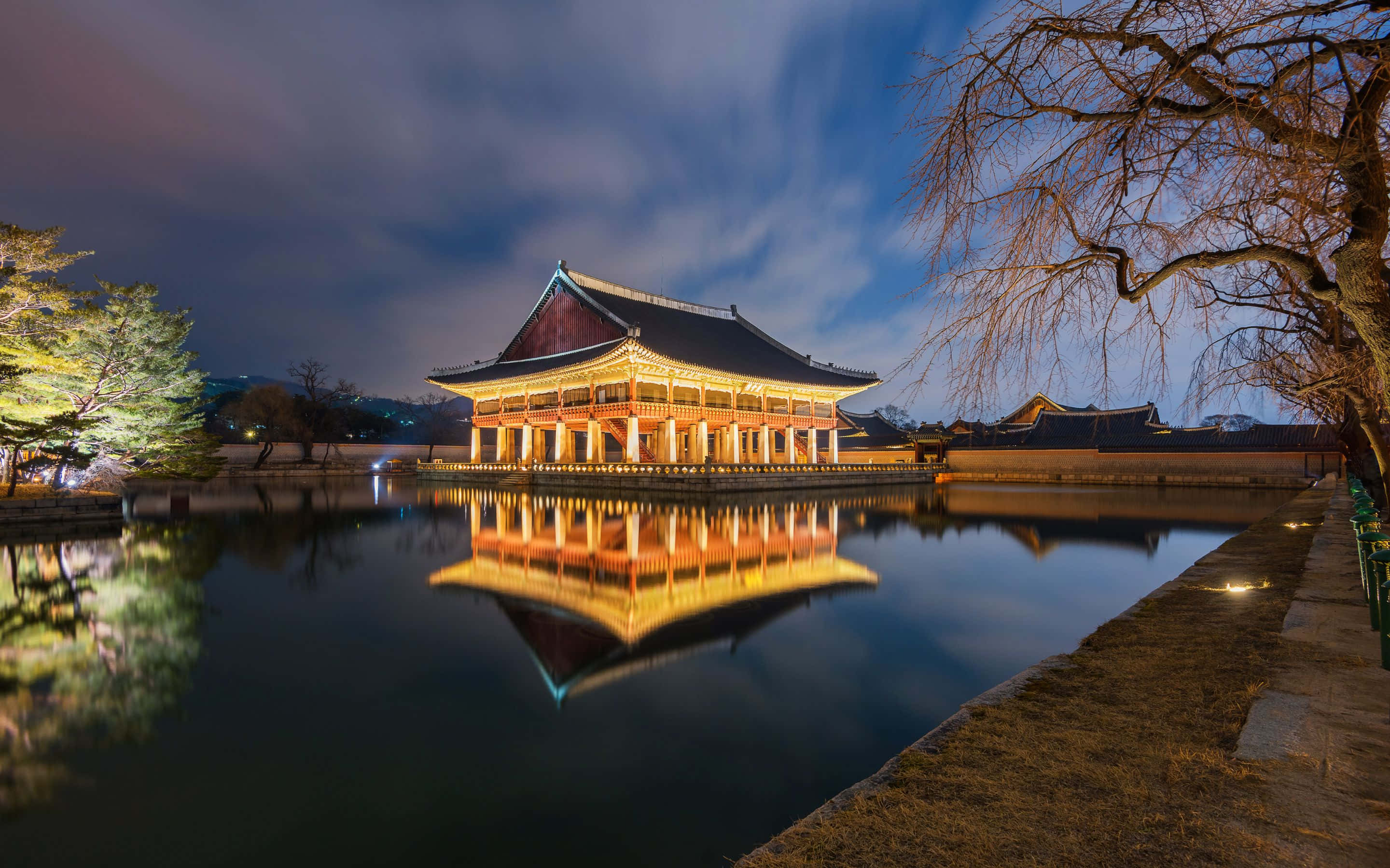 2880x1800 桌布 壁紙 — 一座傳統韓國宮殿建築在夜晚溫暖地發光，其倒影完美地映照在昏暗天空下的平靜池塘中。