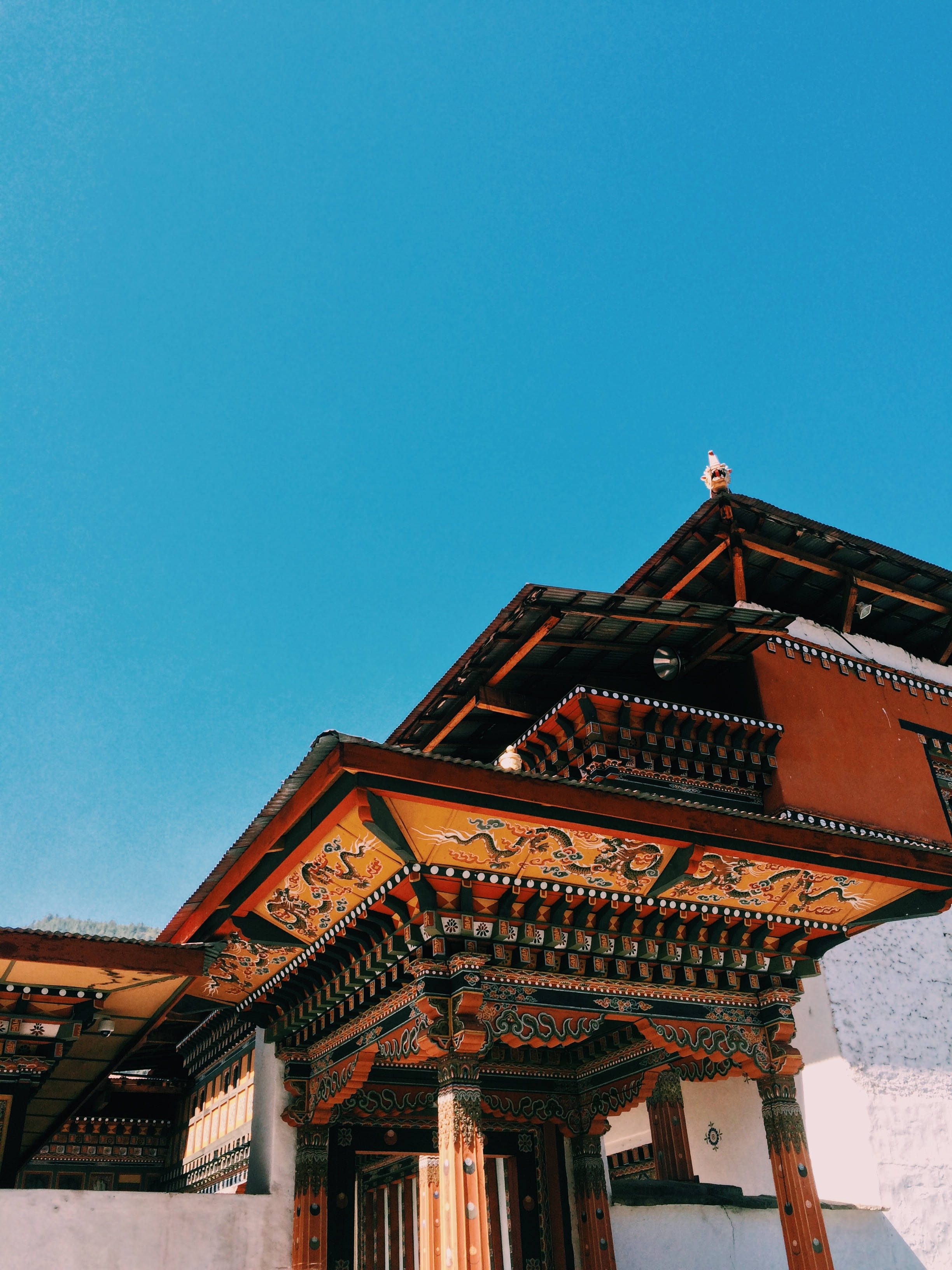 Bhutan 桌布 壁紙 — 一座充滿活力的傳統不丹寺廟，擁有華麗的木雕和紅牆，矗立在清澈的藍天下。