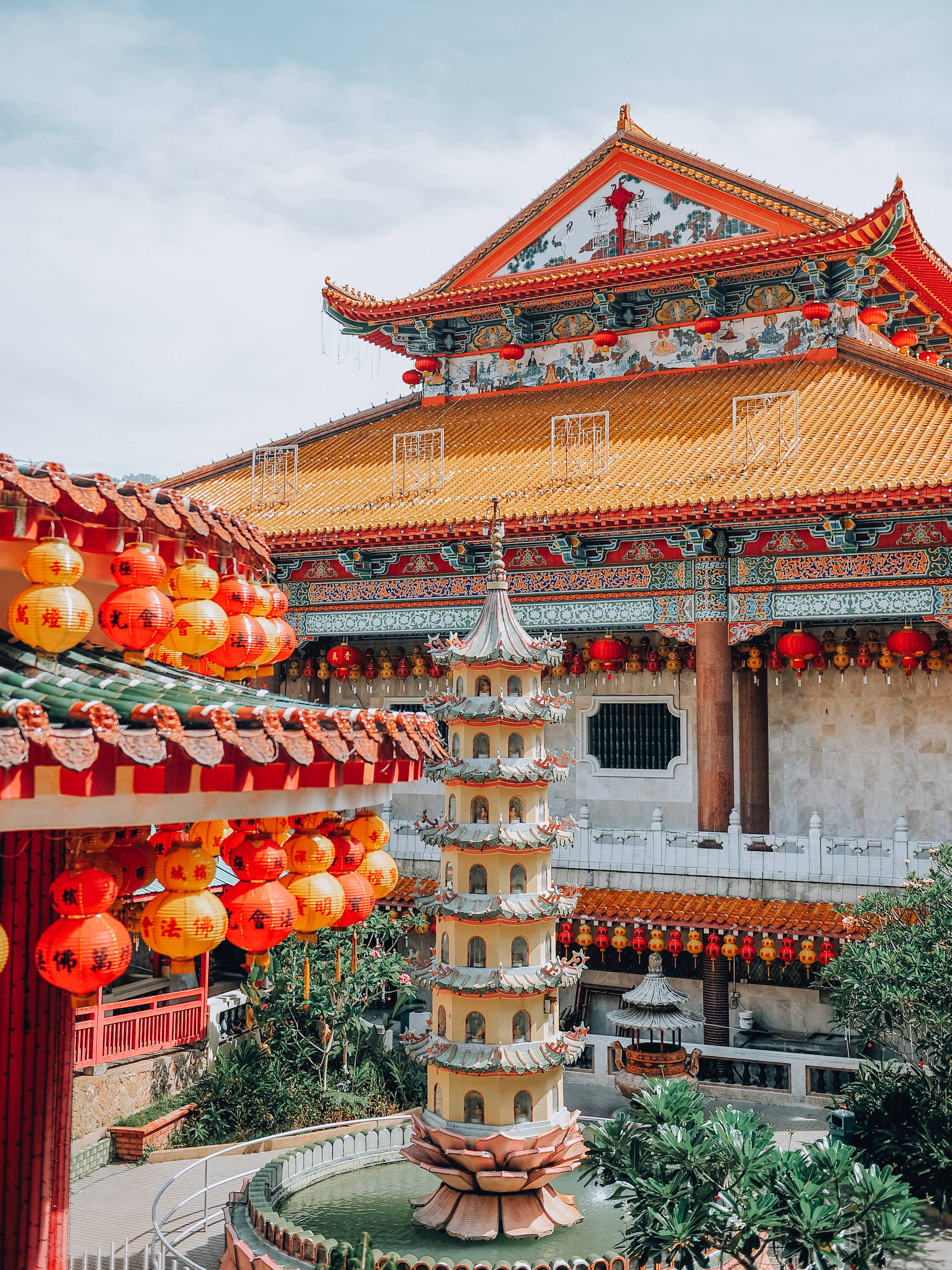 春節 桌布 壁紙 — 一座充滿活力的傳統中國寺廟，擁有華麗的橙色屋頂和紅色燈籠，環繞著中央的寶塔噴泉。