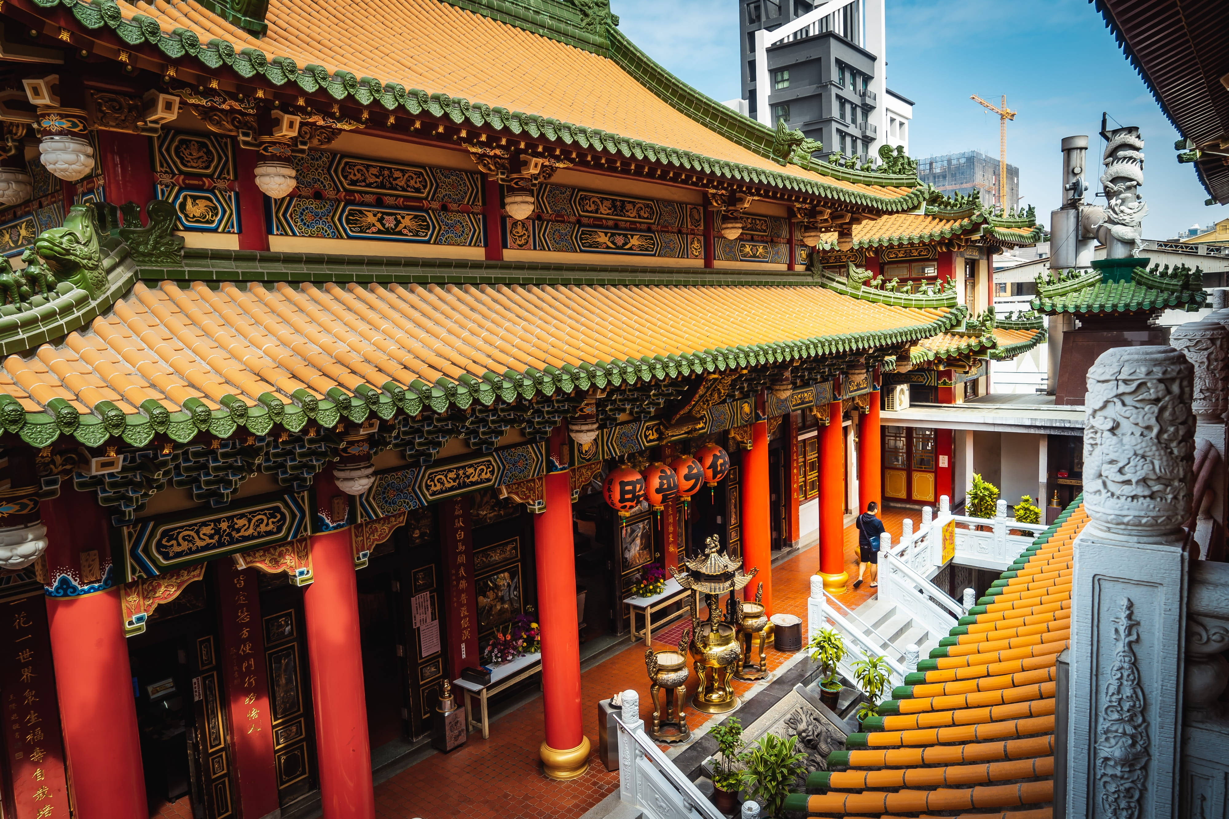 台灣 桌布 壁紙 — 一座充滿活力的傳統中式寺廟，擁有華麗的金色屋頂、紅色柱子和精緻的雕刻，坐落在現代摩天大樓旁。