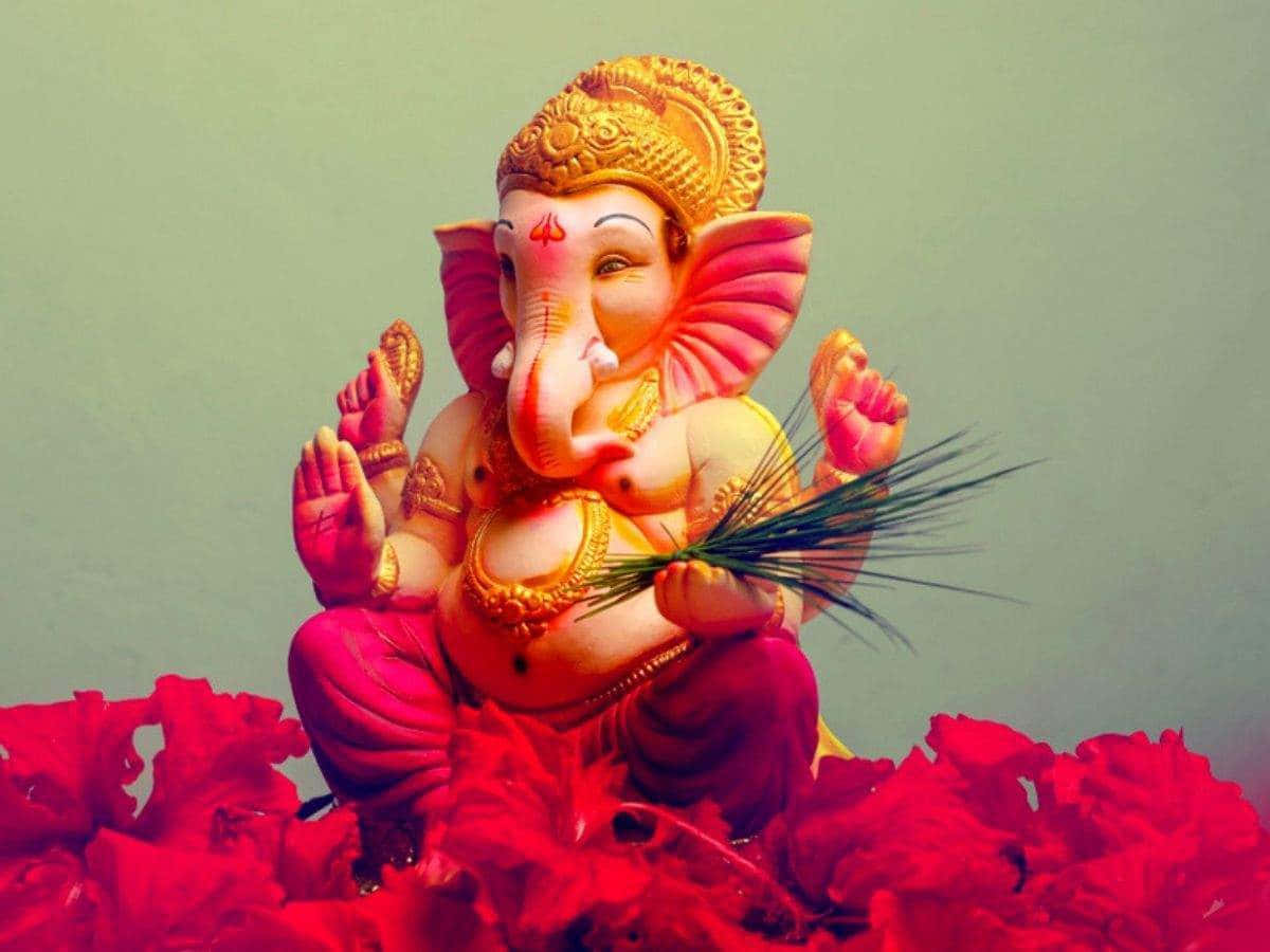 Ganesh 桌布 壁紙 — 一座充滿活力的粉紅和金色象神雕像，安詳地坐在紅色花朵上，背景是柔和的綠色。