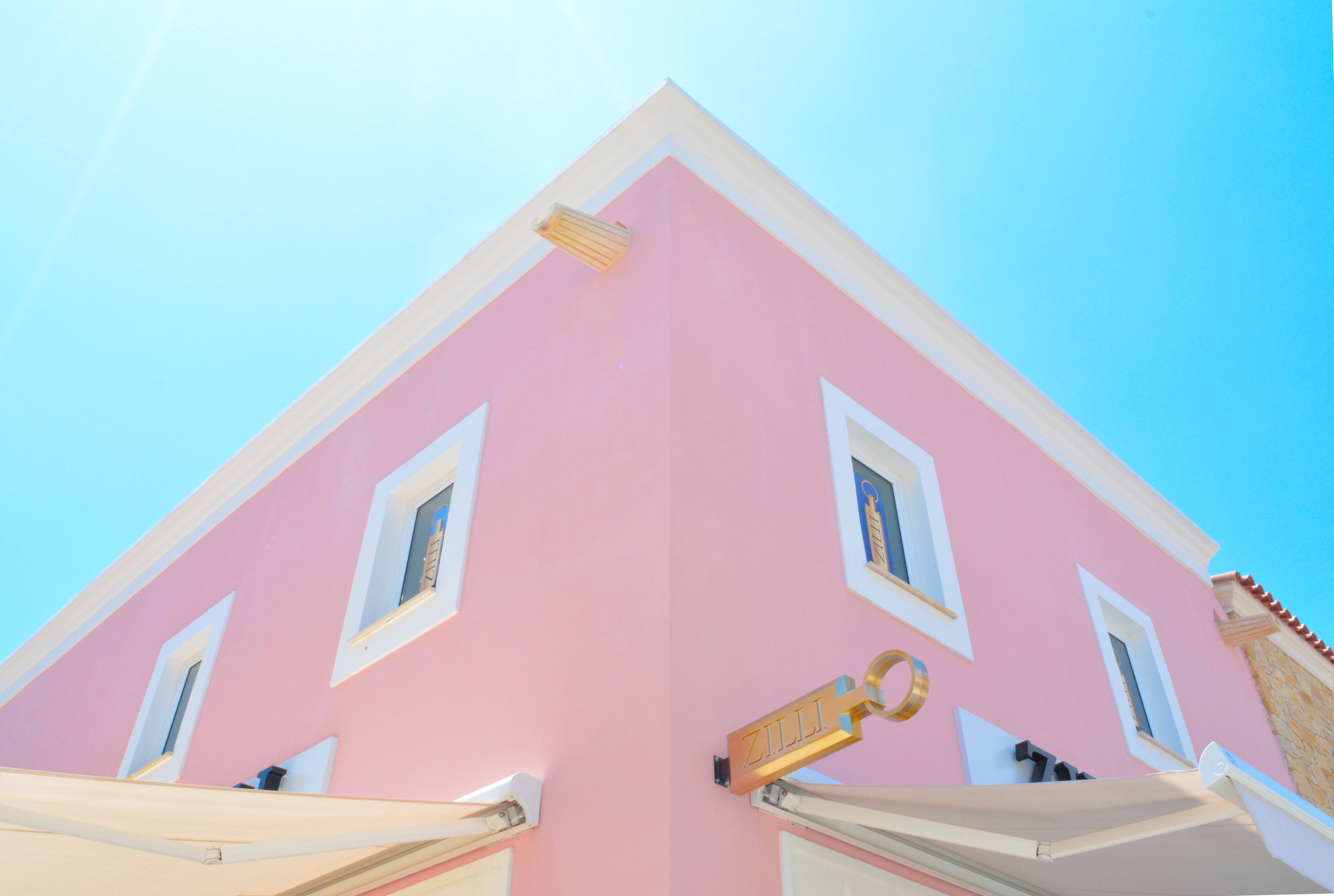 Building 桌布 壁紙 — 一座充滿活力的粉紅色建築，帶有白色飾邊和遮陽篷，矗立在晴朗的藍天下，帶有太陽耀斑。