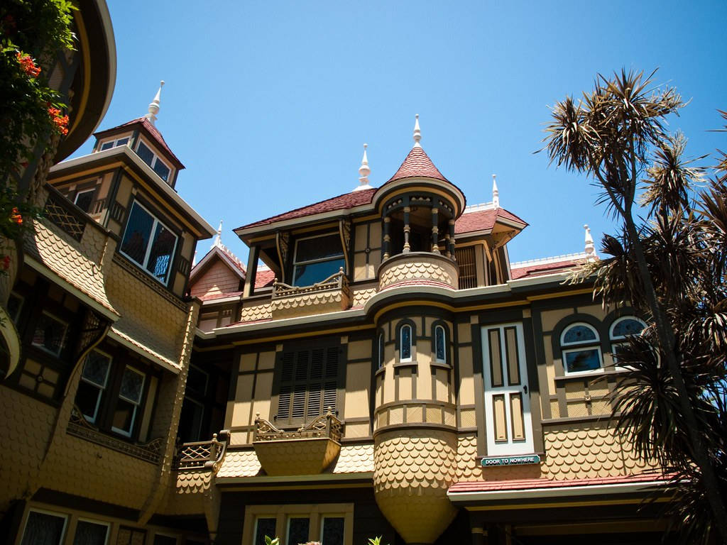 Mansion 桌布 壁紙 — 一座充滿活力的維多利亞式豪宅，帶有華麗的塔樓和鱗片狀木瓦，矗立在晴朗的藍天下，棕櫚樹環繞。