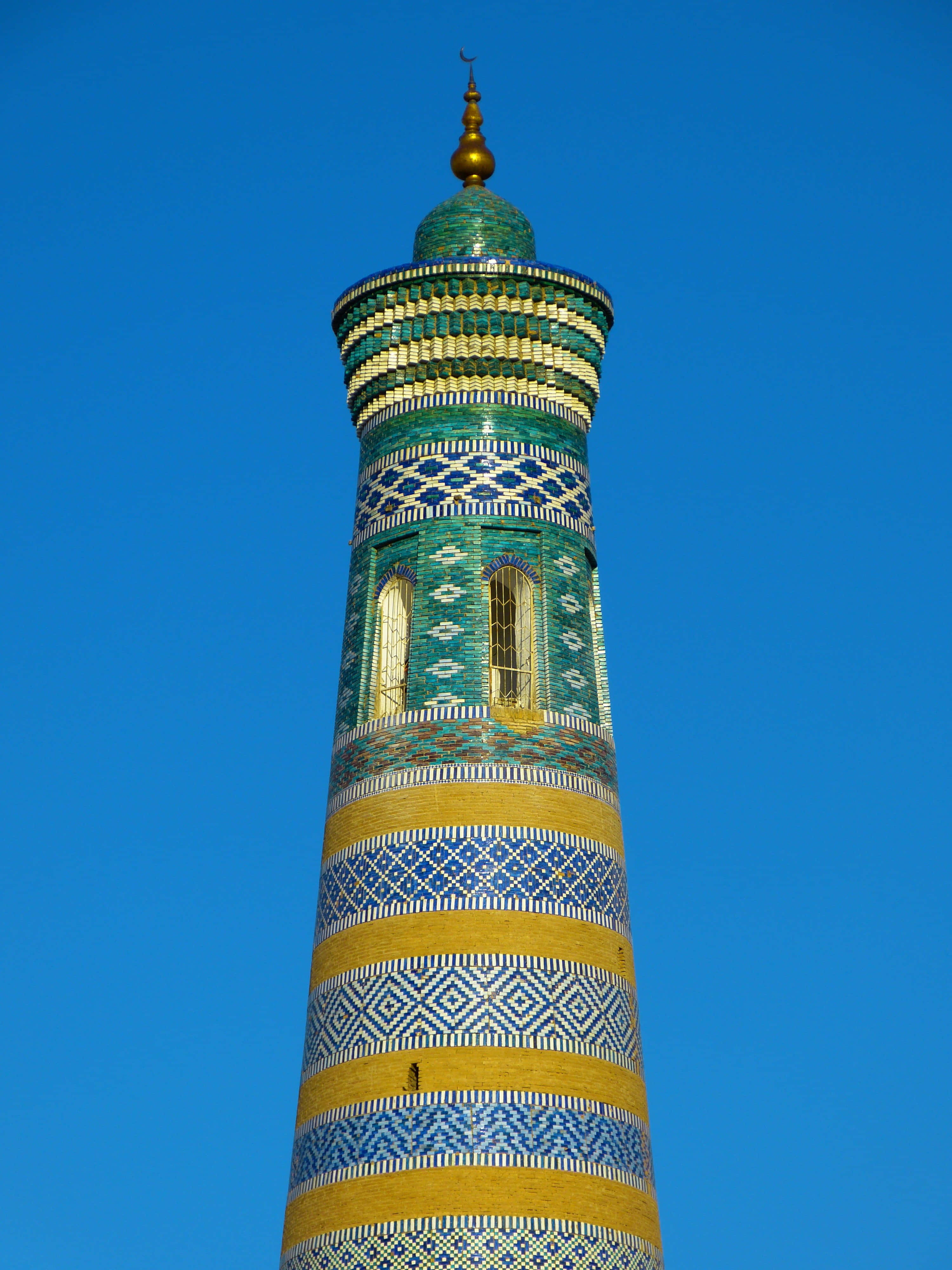 Uzbekistan 桌布 壁紙 — 一座充滿活力的藍綠色和金色瓷磚宣禮塔，在晴朗的藍天下，帶有複雜的幾何圖案。