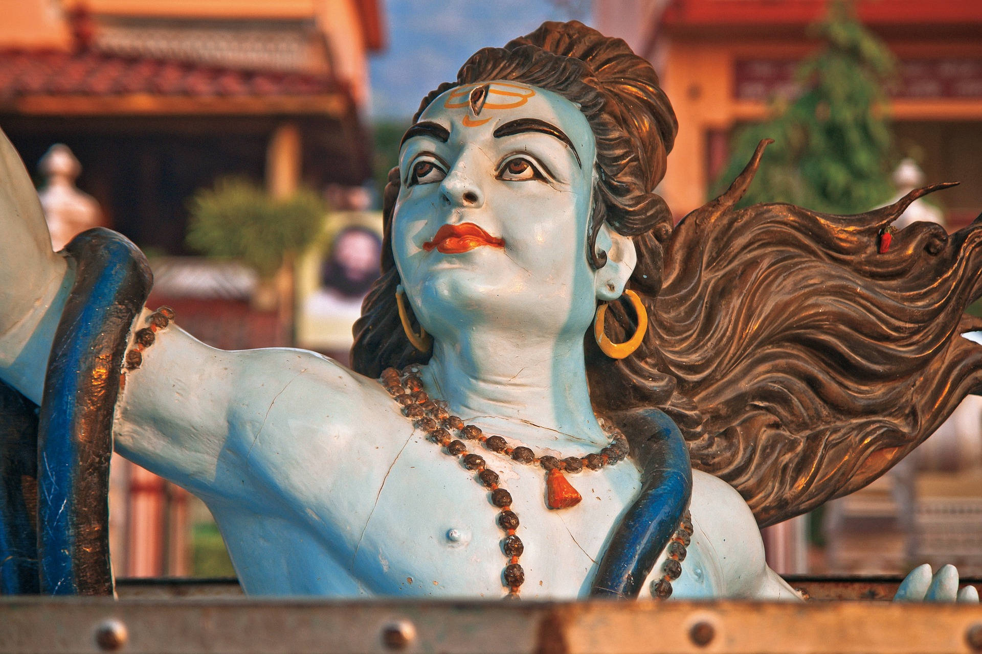 shiv shankar 桌布 壁紙 — 一座充滿活力的藍色印度教神像，擁有飄逸的棕色頭髮和紅色嘴唇，矗立在寺廟環境中。