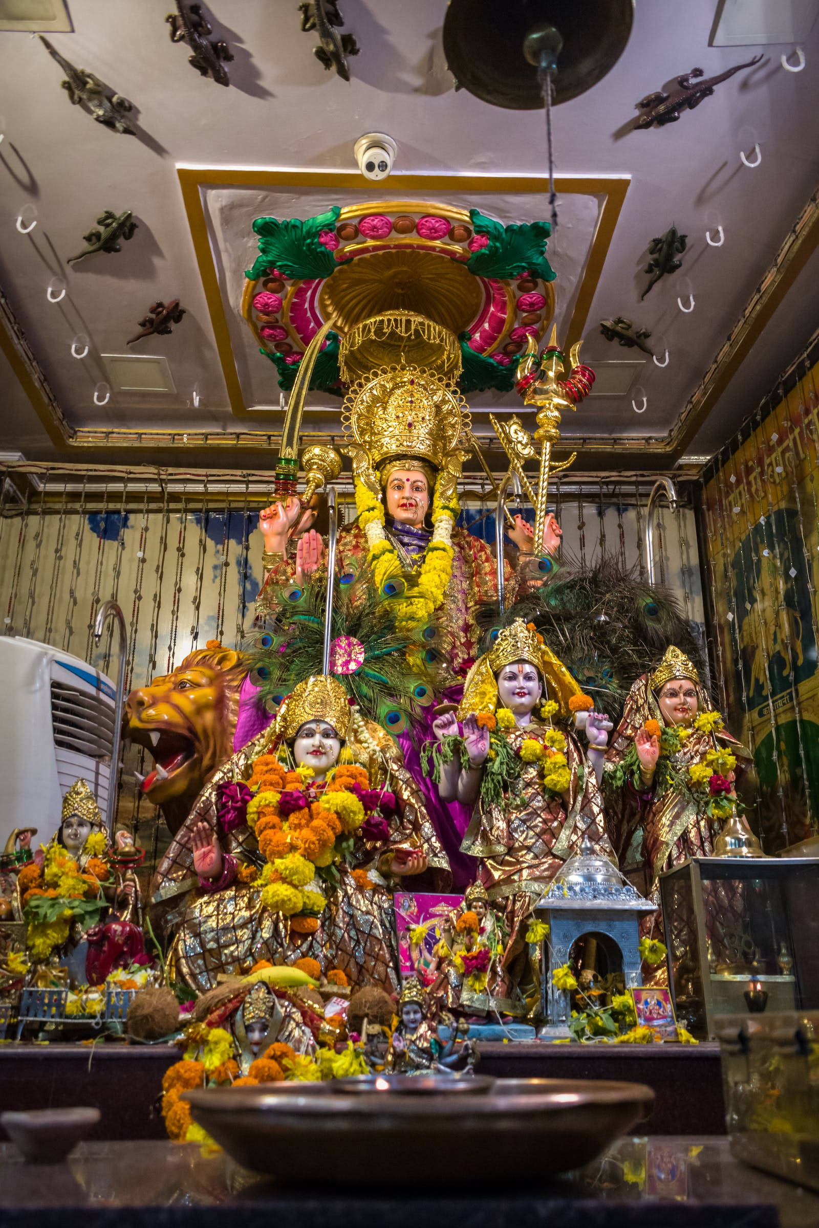 maa durga 桌布 壁紙 — 一座充滿活力的金色神像，飾有鮮花，周圍環繞著較小的神像，位於裝飾華麗的寺廟神龕中。