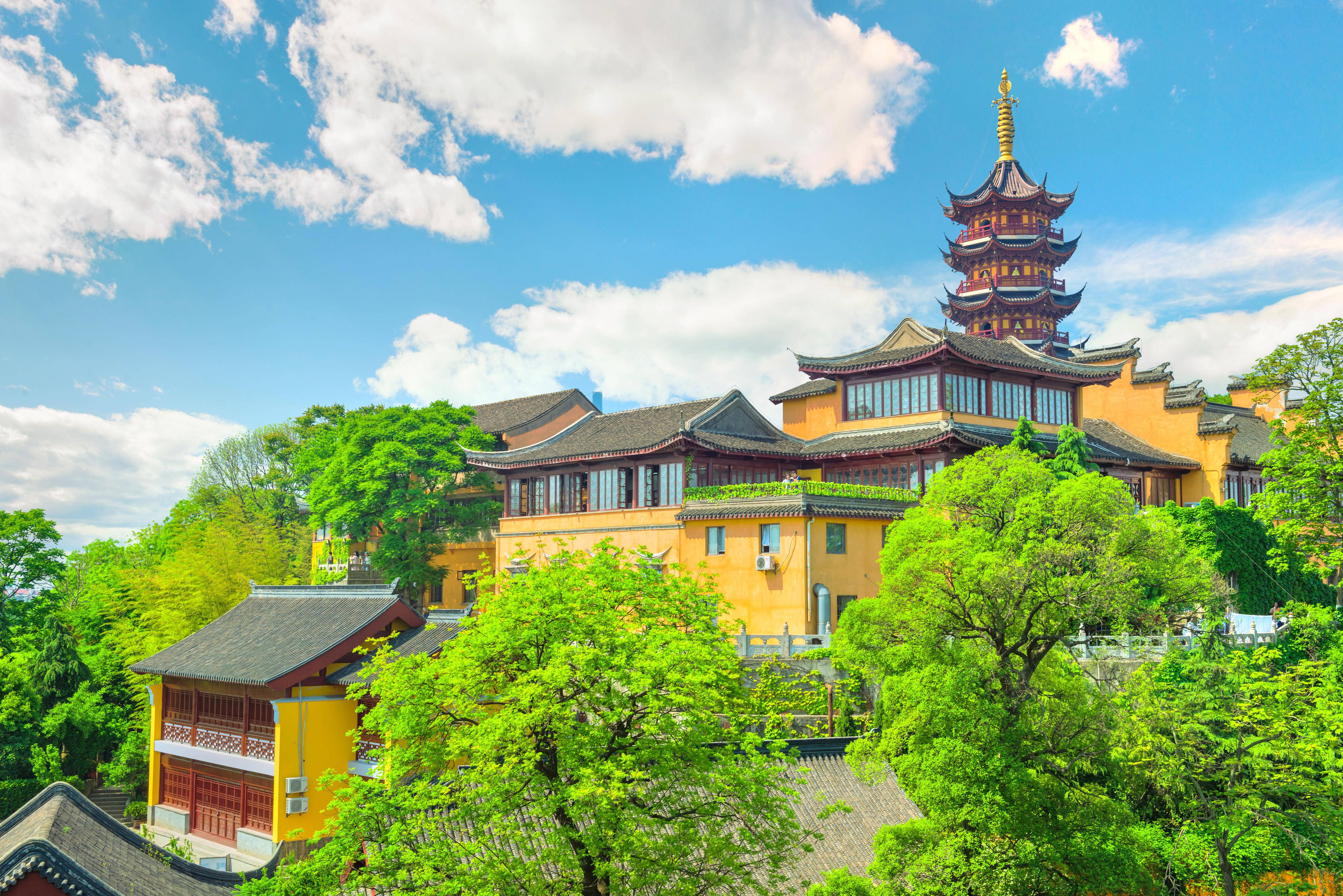 Nanjing 桌布 壁紙 — 一座充滿活力的黃色寶塔和寺廟建築群，坐落在茂密的綠樹之中，上方是晴朗的藍天和蓬鬆的白雲。