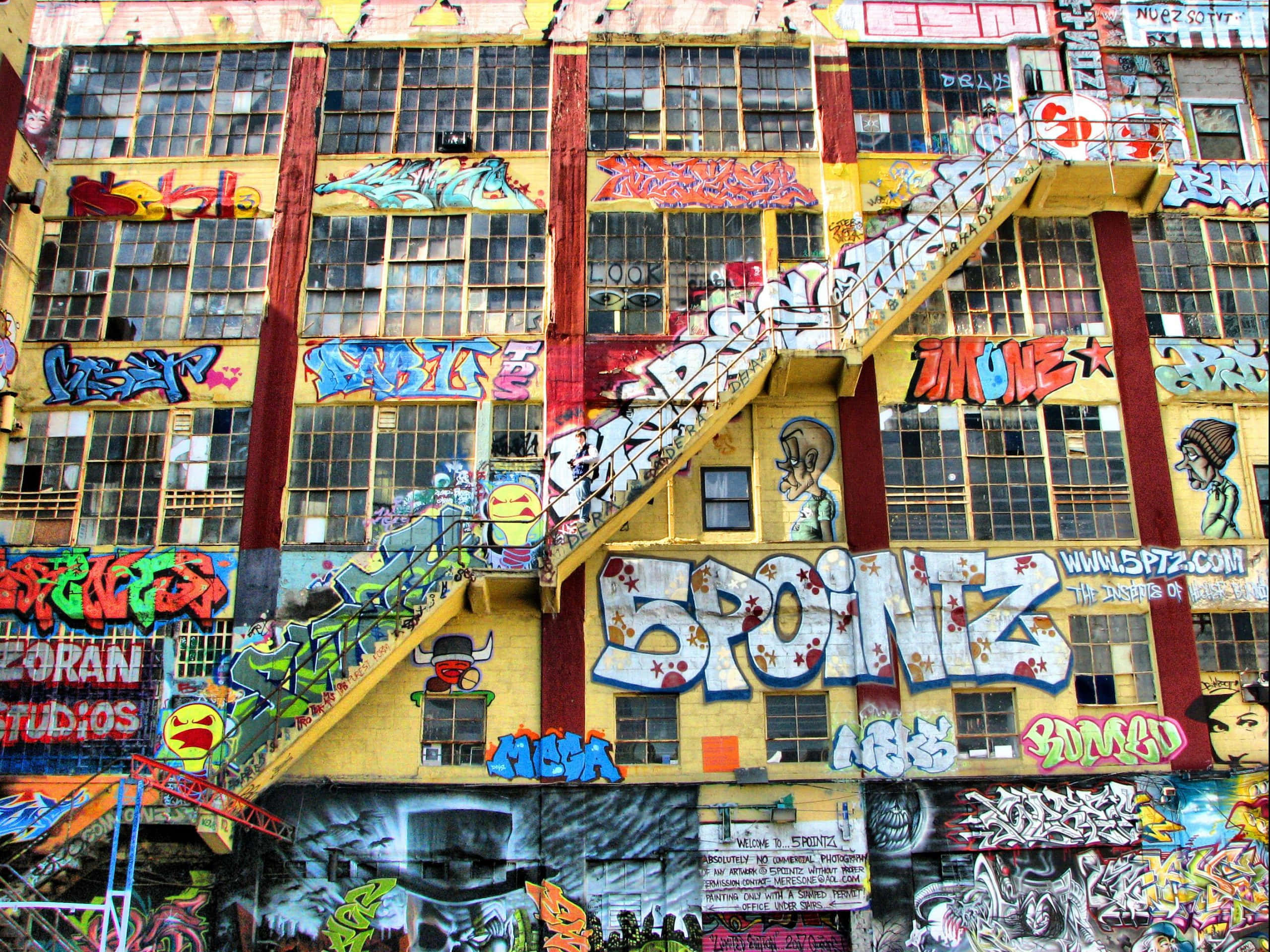 Graffiti Art 桌布 壁紙 — 一座充滿活力的黃色建築，覆蓋著色彩繽紛的塗鴉和大膽的街頭藝術，逃生樓梯蜿蜒而上其外牆。