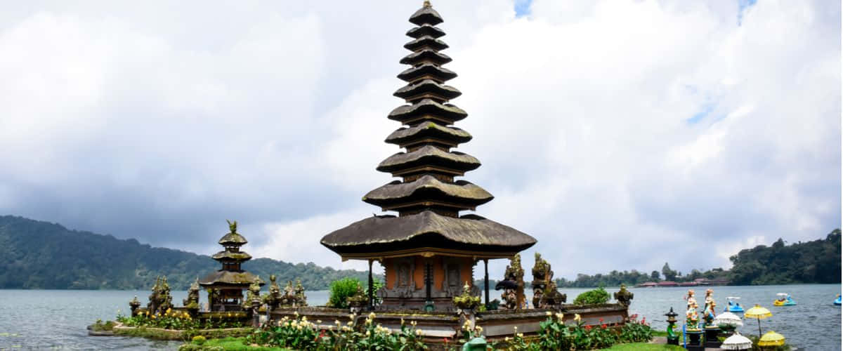 Bali Island 桌布 壁紙 — 一座分層的峇里島寺廟優雅地矗立在湖面上，四周是鬱鬱蔥蔥的綠色山丘，天空多雲。