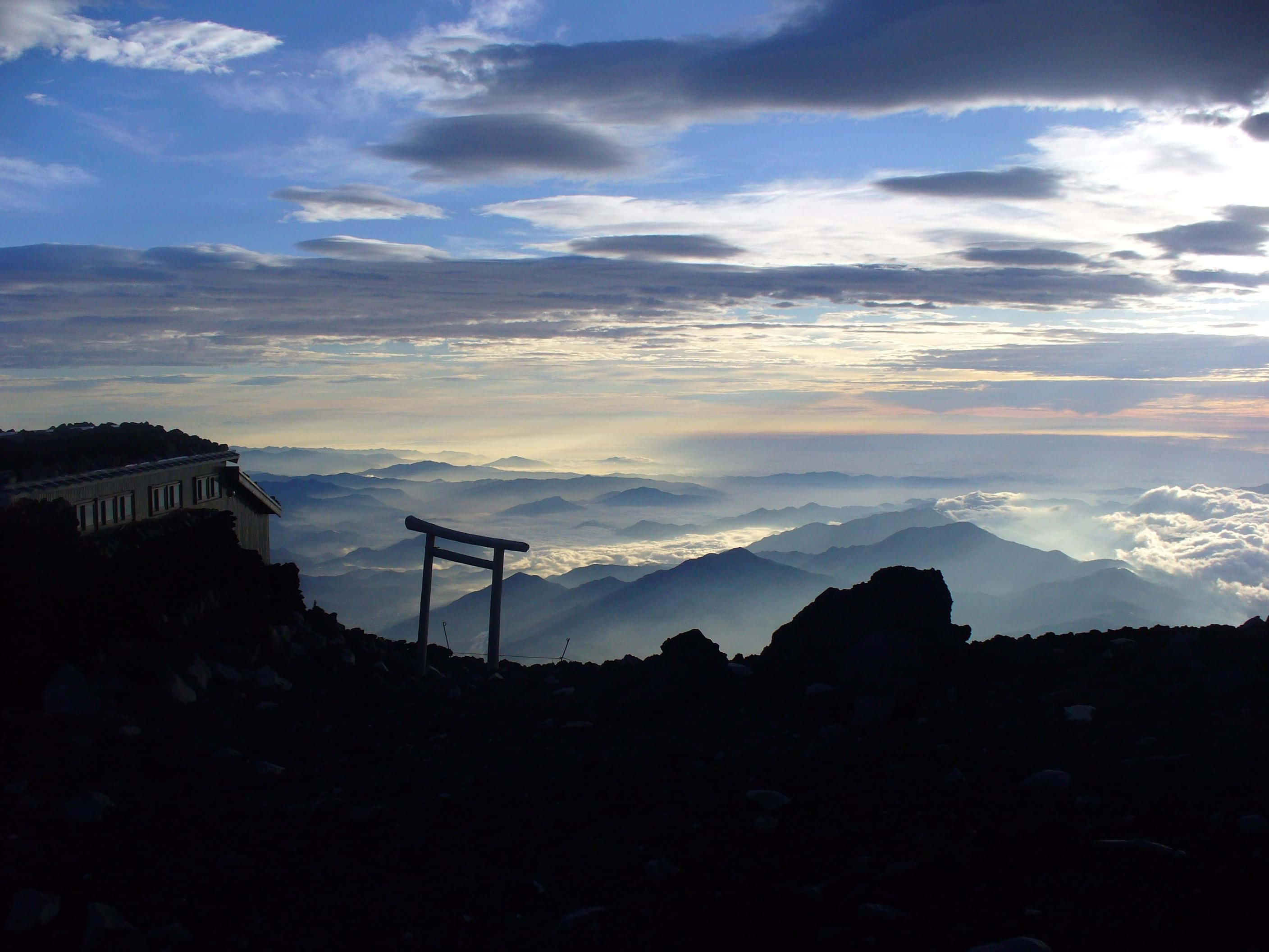 Mt Fuji 桌布 壁紙 — 一座剪影的鳥居矗立在山頂上，俯瞰日出時的雲海，層層山脈逐漸消失在霧氣中。