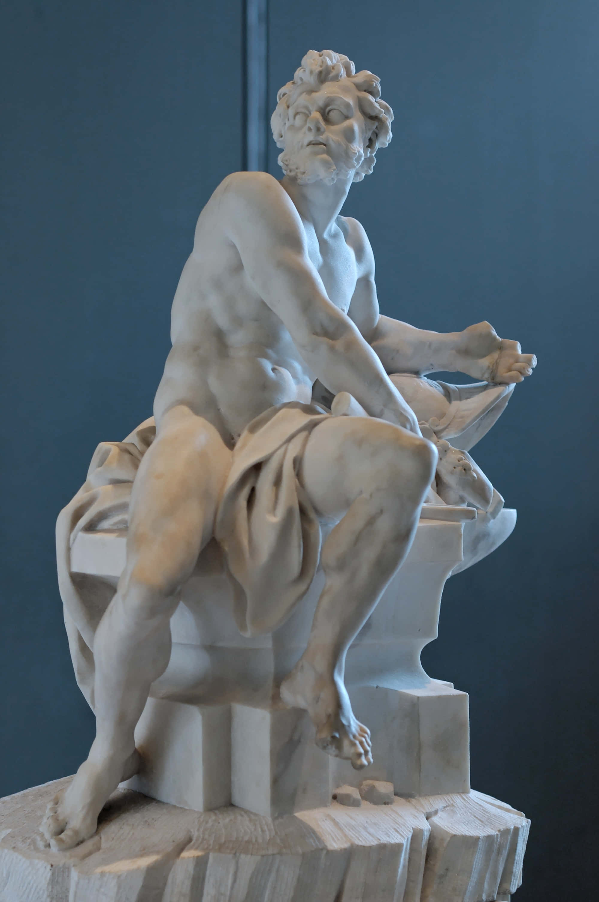 greek 桌布 壁紙 — 一座古典大理石雕像，描繪一位肌肉發達的裸體男性動態地坐在帶有垂布裝飾的基座上。