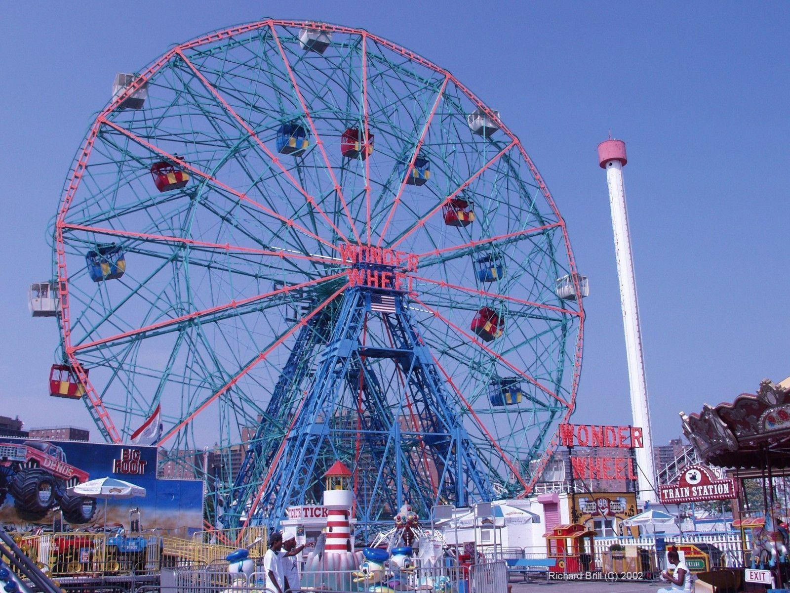美學 桌布 壁紙 — 一座名為 Wonder Wheel 的藍紅相間高聳摩天輪，在熙攘的遊樂園中襯著清澈的藍天。