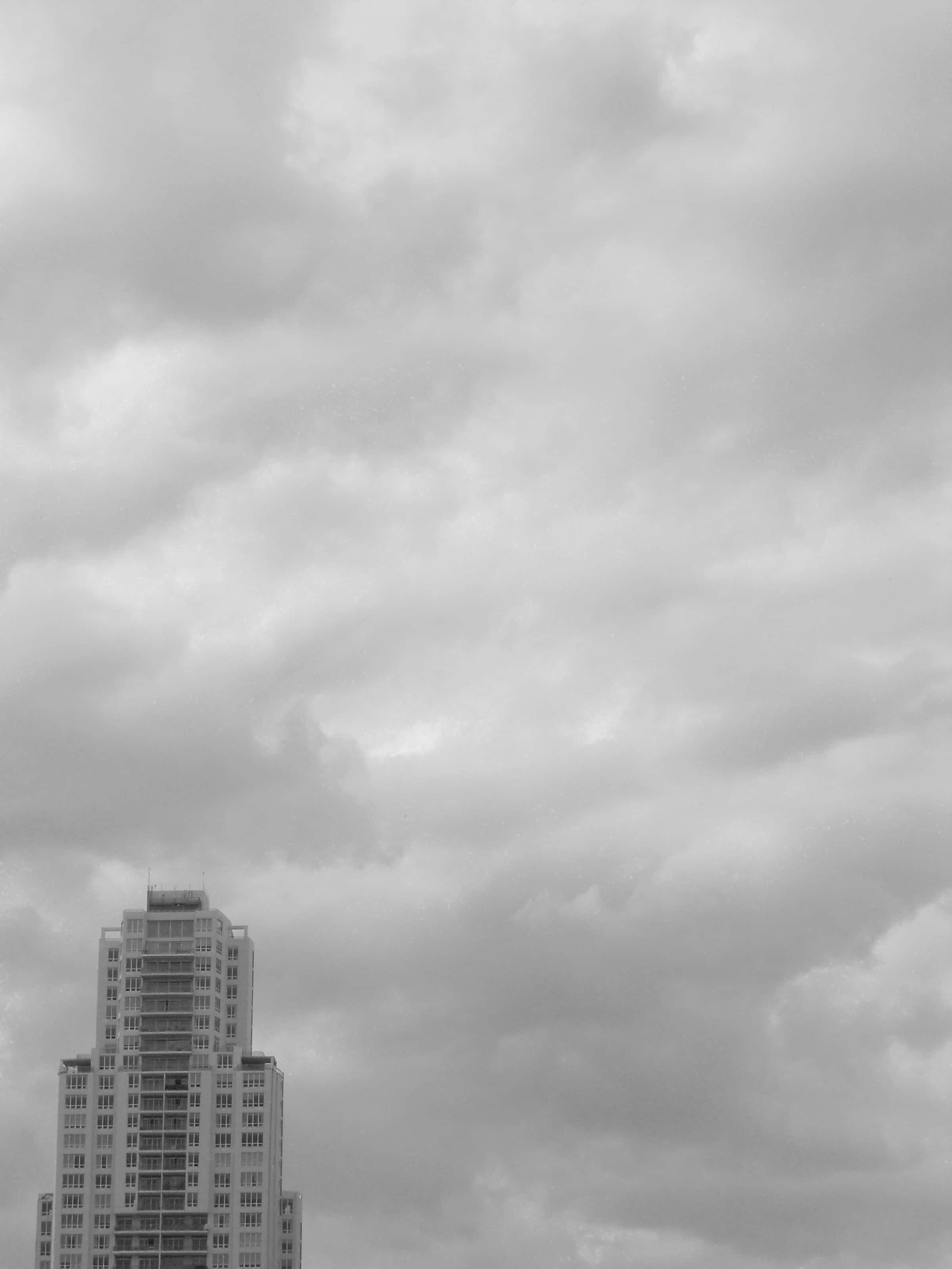 Black And White Sky 桌布 壁紙 — 一座單色摩天大樓刺穿密集的陰天，帶有戲劇性的雲層紋理。