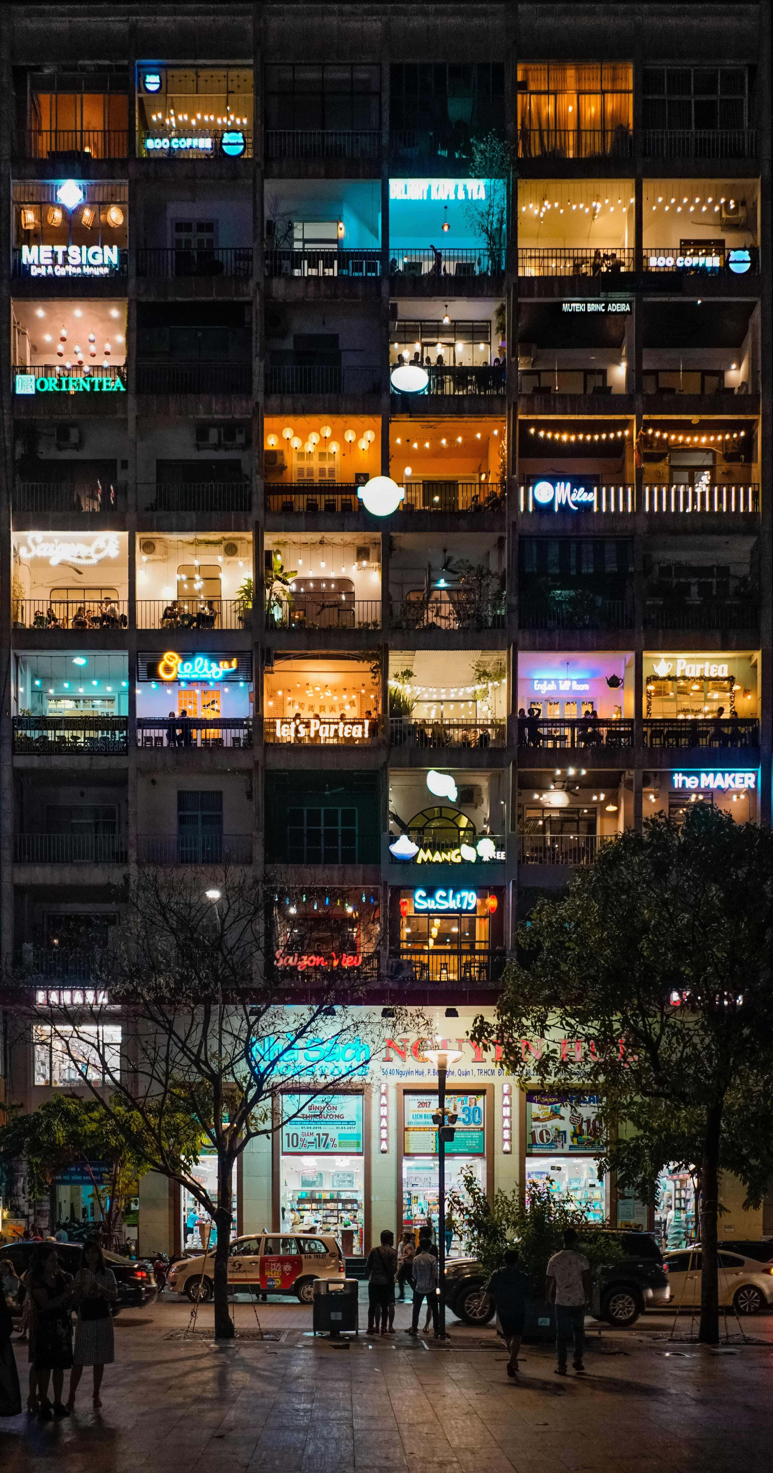 iPhone 桌布 壁紙 — 一座多層建築的充滿活力的夜景，發光的咖啡館和商店櫥窗照亮了下方的城市街道。