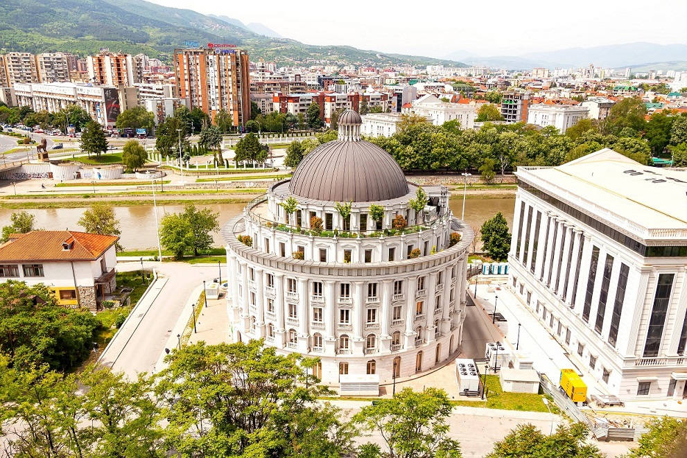 城市 桌布 壁紙 — 一座大型白色圓頂建築，屋頂有綠植，俯瞰河流和城市景觀，四周環繞著鬱鬱蔥蔥的綠色山丘。