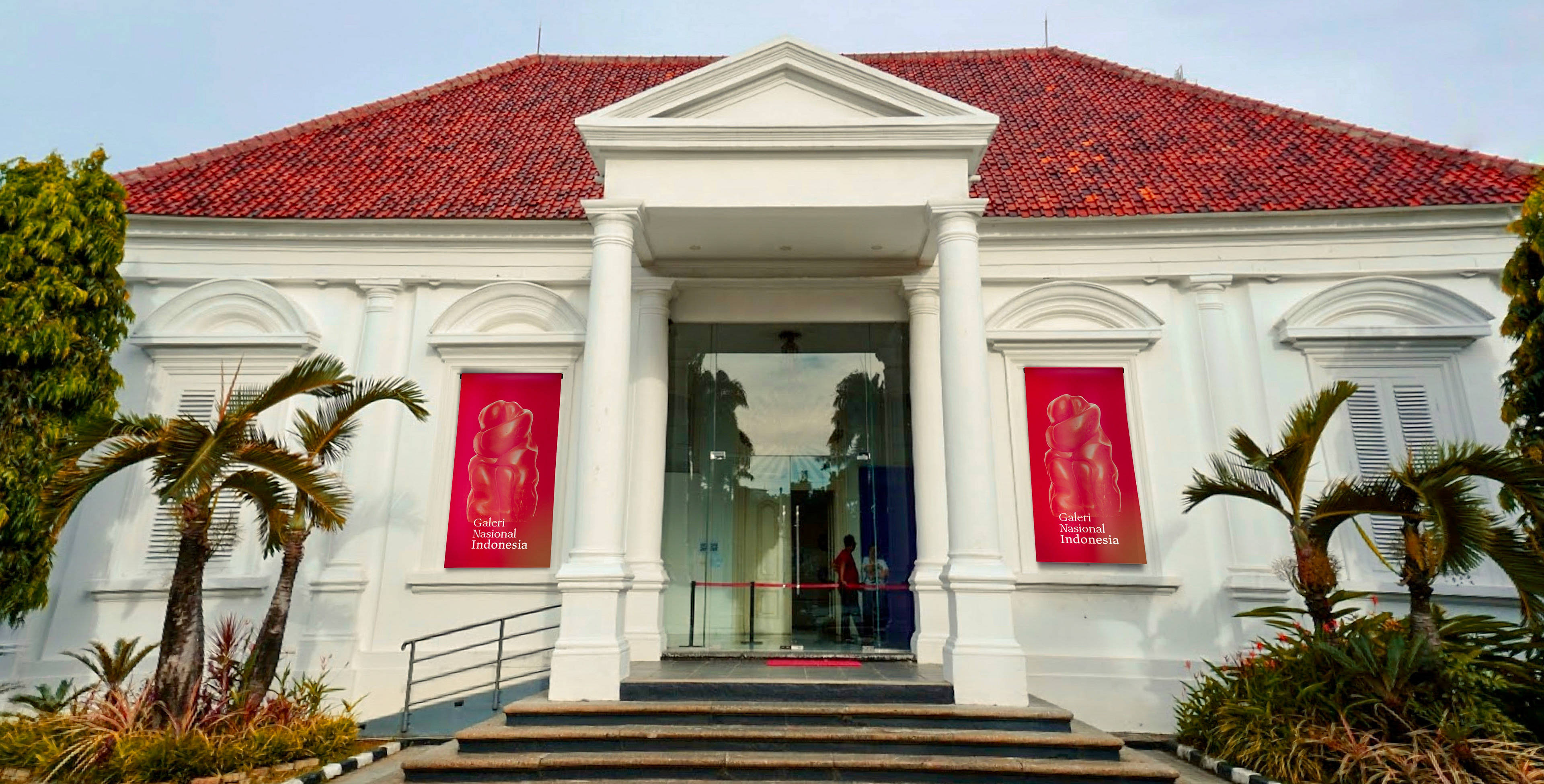 Jakarta 桌布 壁紙 — 一座大型白色殖民風格建築，擁有紅色瓦片屋頂和玻璃入口，兩旁種植棕櫚樹，天空晴朗。