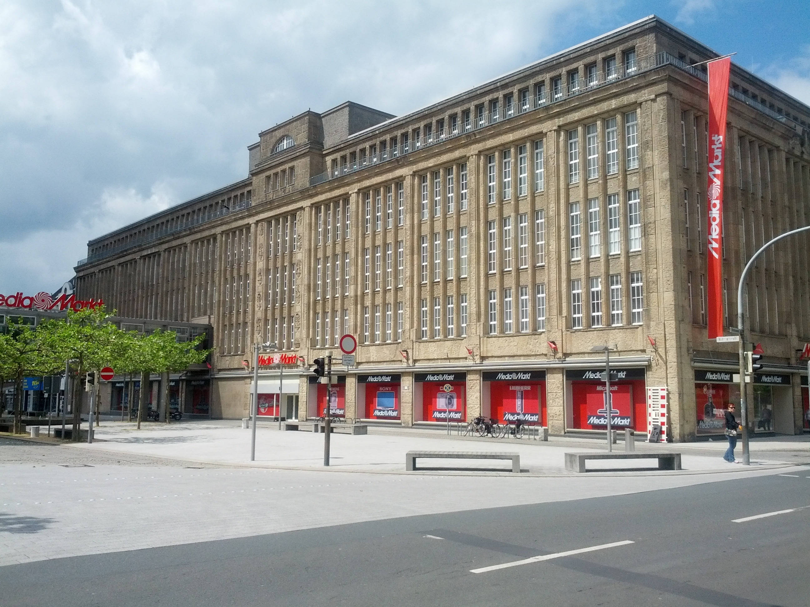 Building 桌布 壁紙 — 一座大型石建築，帶有紅色Media Markt店面，天空部分多雲。