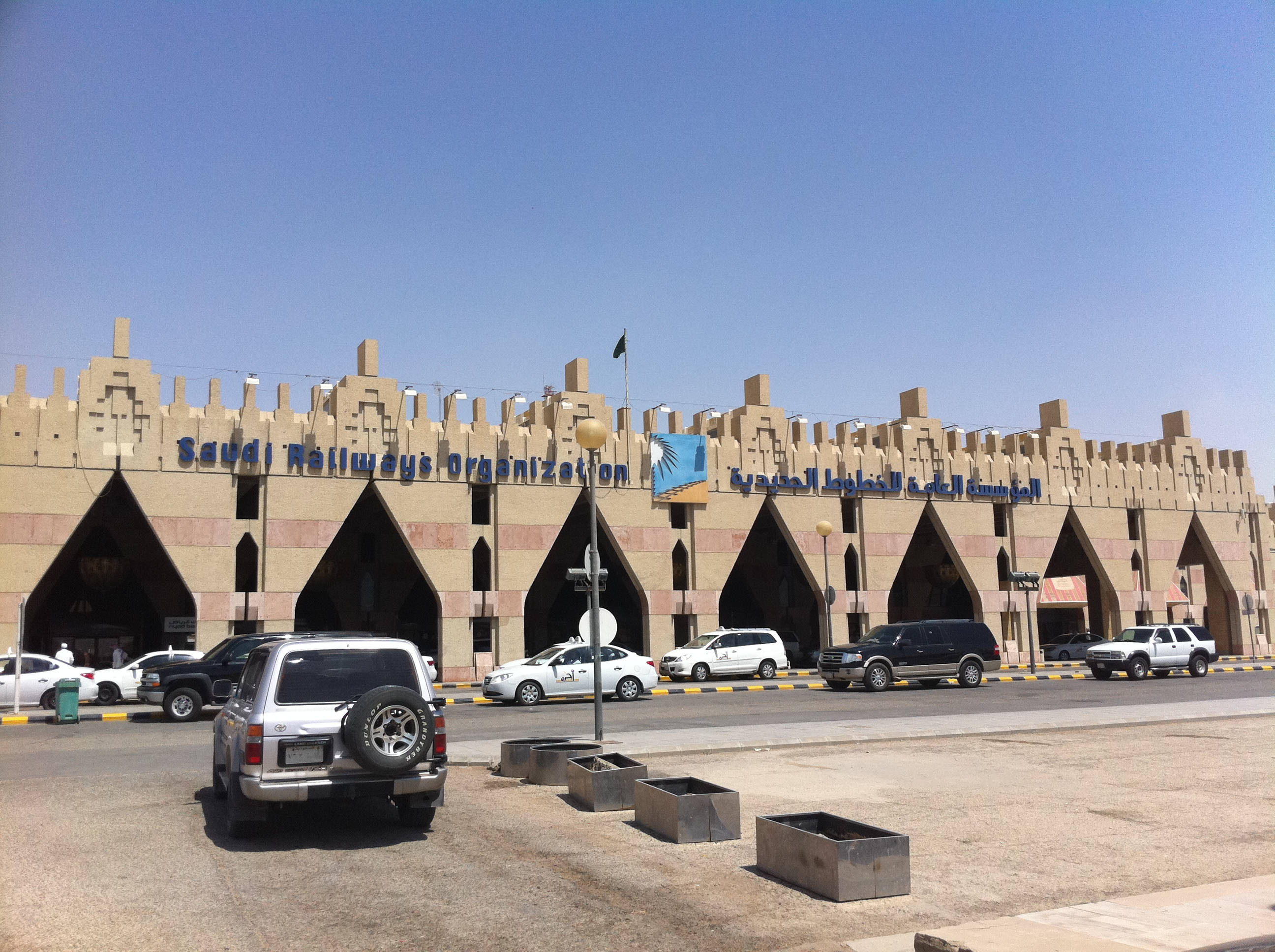 Riyadh 桌布 壁紙 — 一座大型米色建築，設有拱形入口和「Saudi Railways Organization」標誌，在晴朗的藍天下，前面停有汽車。