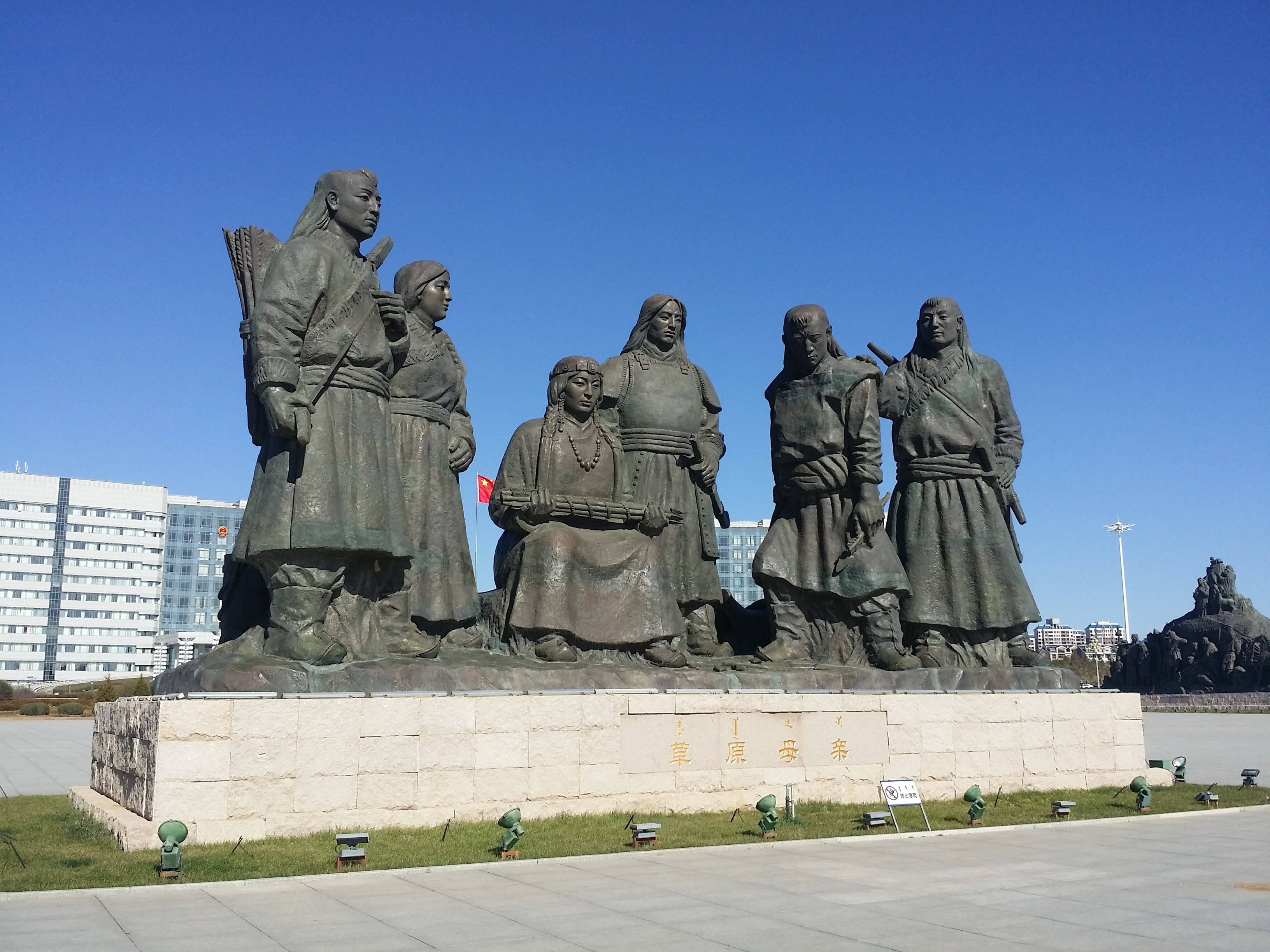 Mongolia 桌布 壁紙 — 一座大型青銅雕像，描繪六位傳統蒙古人物，在都市廣場的清澈藍天下傲然矗立。