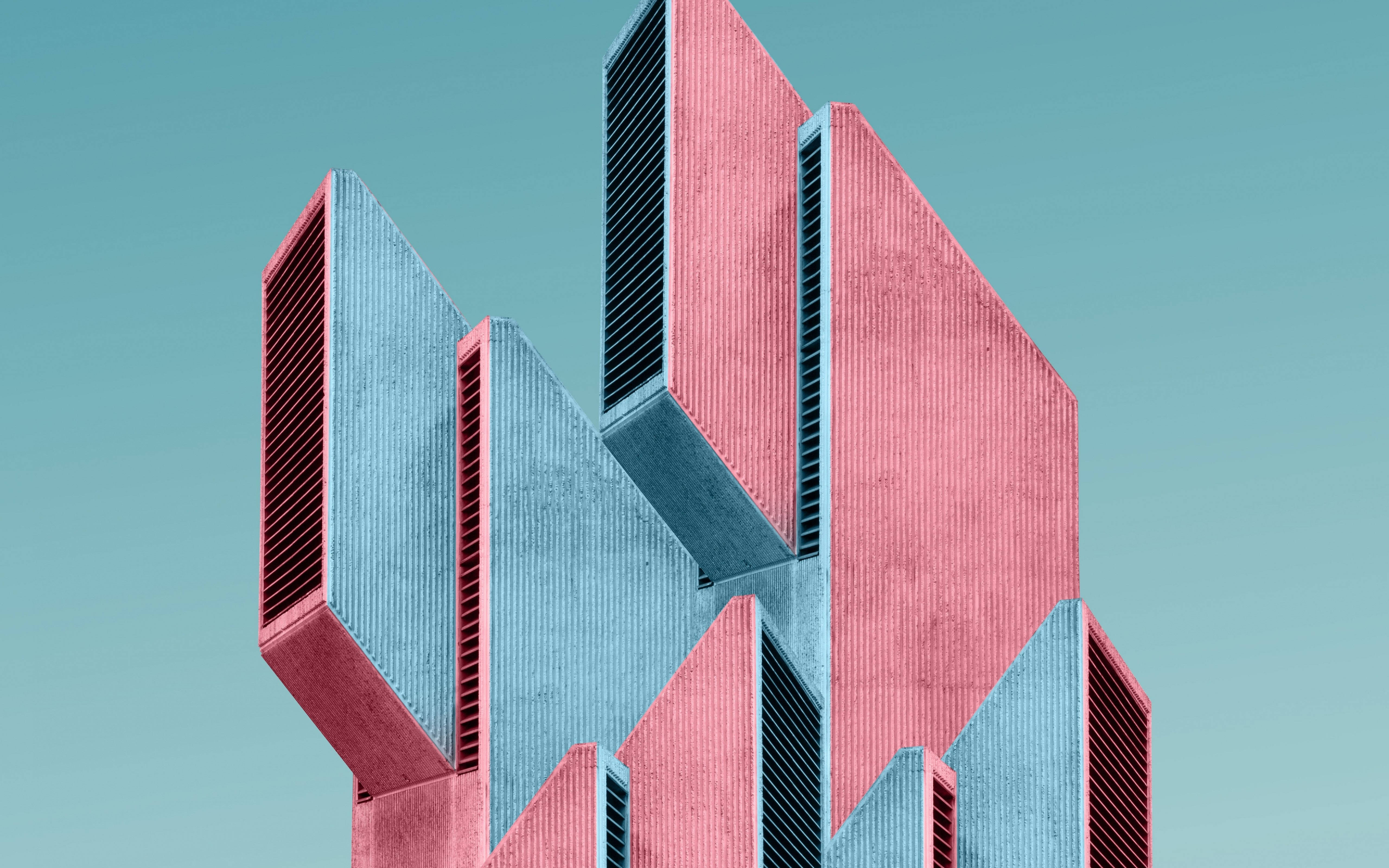 Architecture 桌布 壁紙 — 一座大膽的幾何建築，帶有粉紅色和青綠色的稜角立面，矗立在清澈的青綠色天空下。