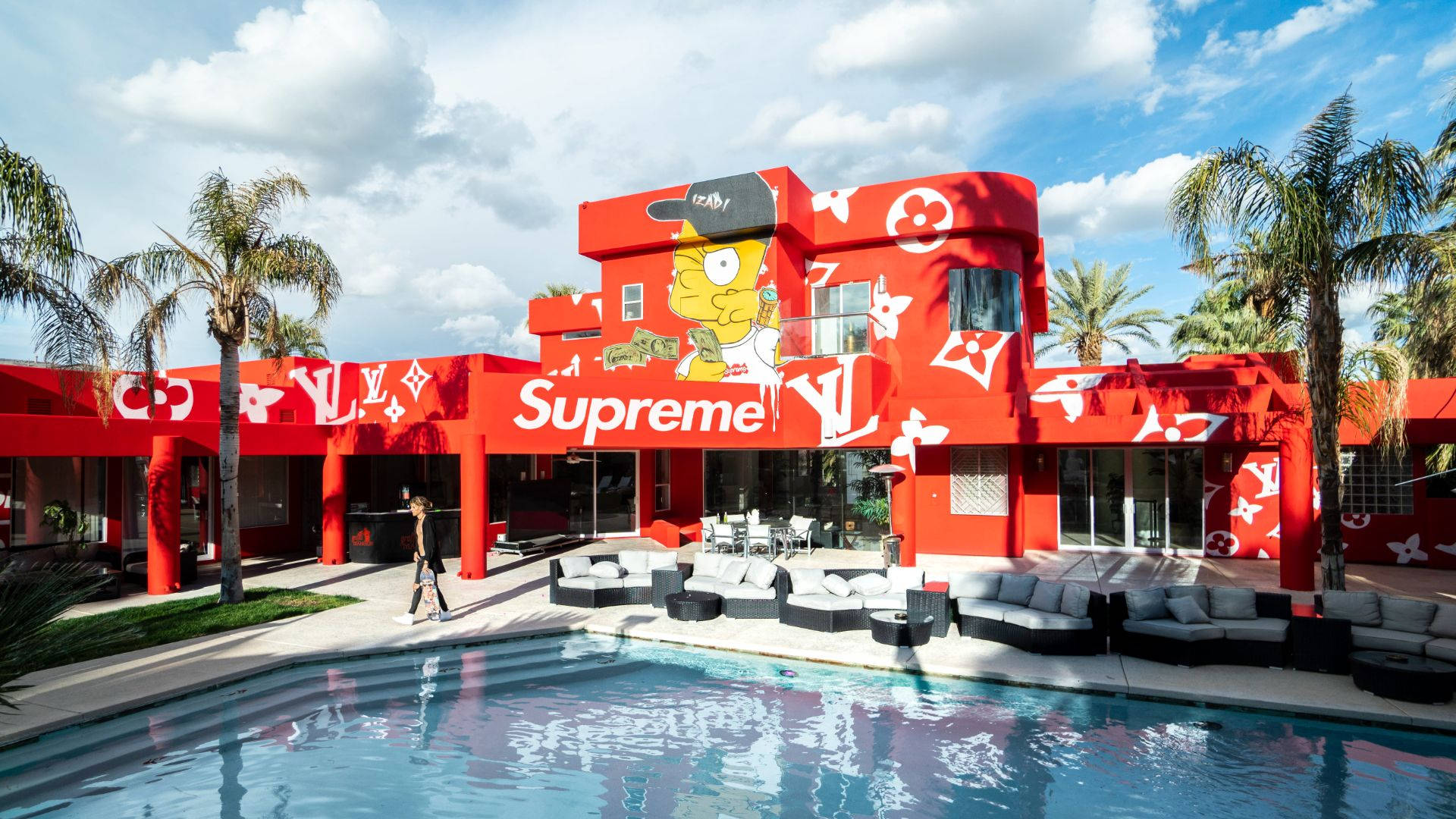 Cool Supreme 桌布 壁紙 — 一座大膽的紅色建築，上面有巨大的辛普森角色和Supreme品牌標誌，旁邊是一個被棕櫚樹環繞的游泳池，天空部分多雲。