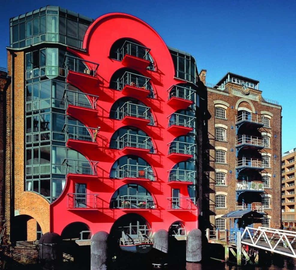 Postmodernism 桌布 壁紙 — 一座大膽的紅色弧形建築，帶有拱形陽台，矗立在運河旁，天空清澈湛藍。