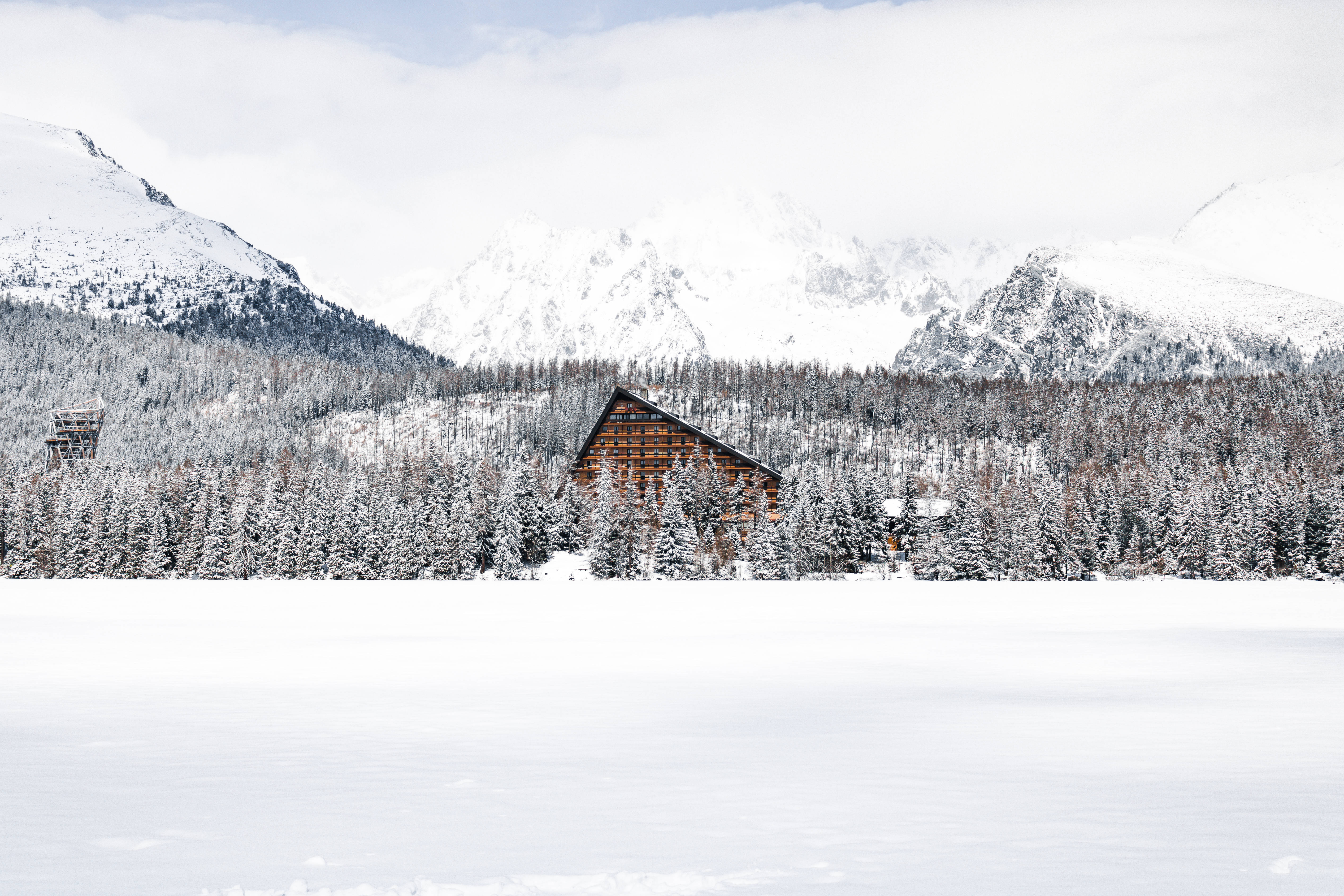 Slovakia 桌布 壁紙 — 一座孤獨的木屋坐落在白雪覆蓋的松樹林中，背景是雄偉的雪山。