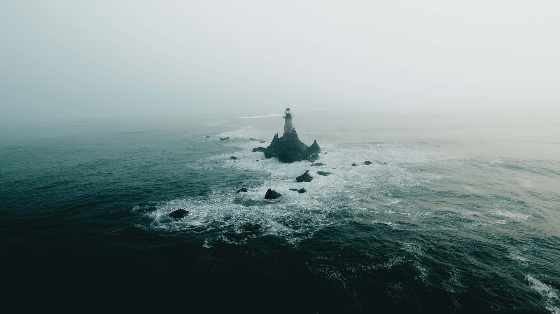 Isolated Lighthouse on a Craggy Islet Amidst Ocean Waves 壁紙 — 一座孤獨的燈塔矗立在岩石小島上，周圍是翻騰的黑暗海洋，天空灰濛濛。