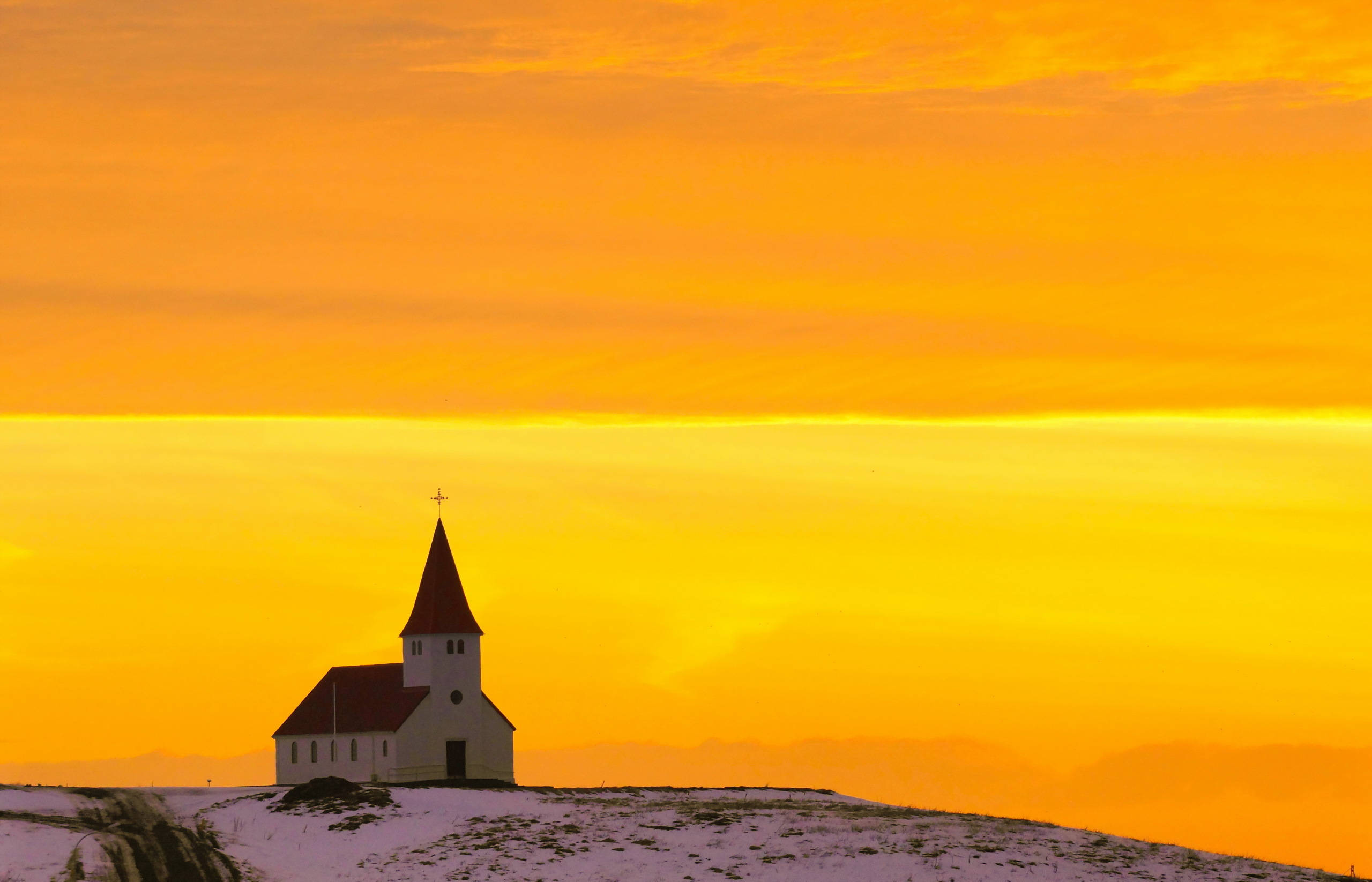 Church 桌布 壁紙 — 一座孤獨的白色教堂，紅色屋頂，矗立在雪丘上，背景是火紅橙黃的日落天空。