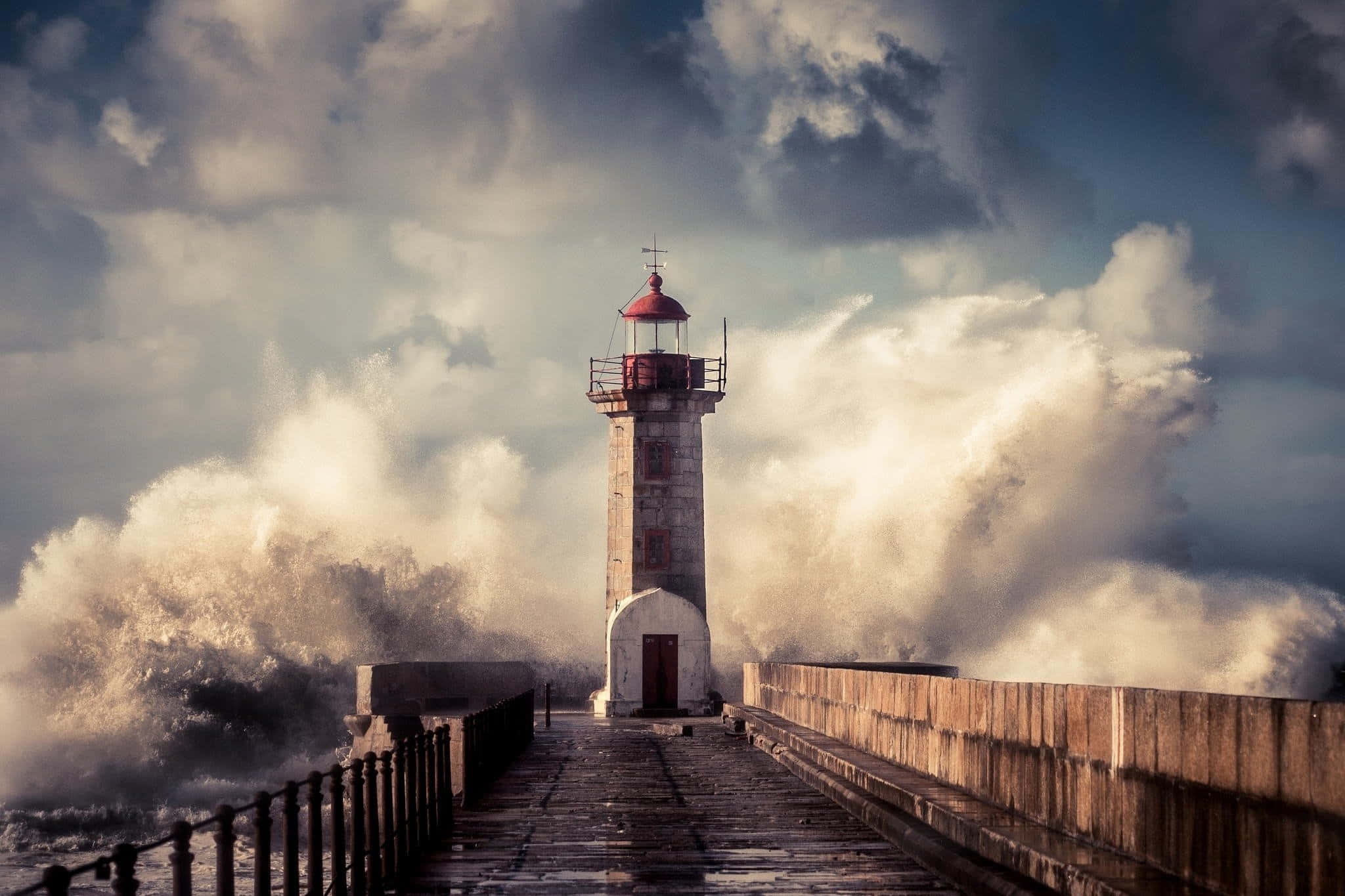 Lighthouse 桌布 壁紙 — 一座孤獨的石燈塔矗立在碼頭上，在暴風雨的天空下，巨大的海浪猛烈地衝擊著它的底部。
