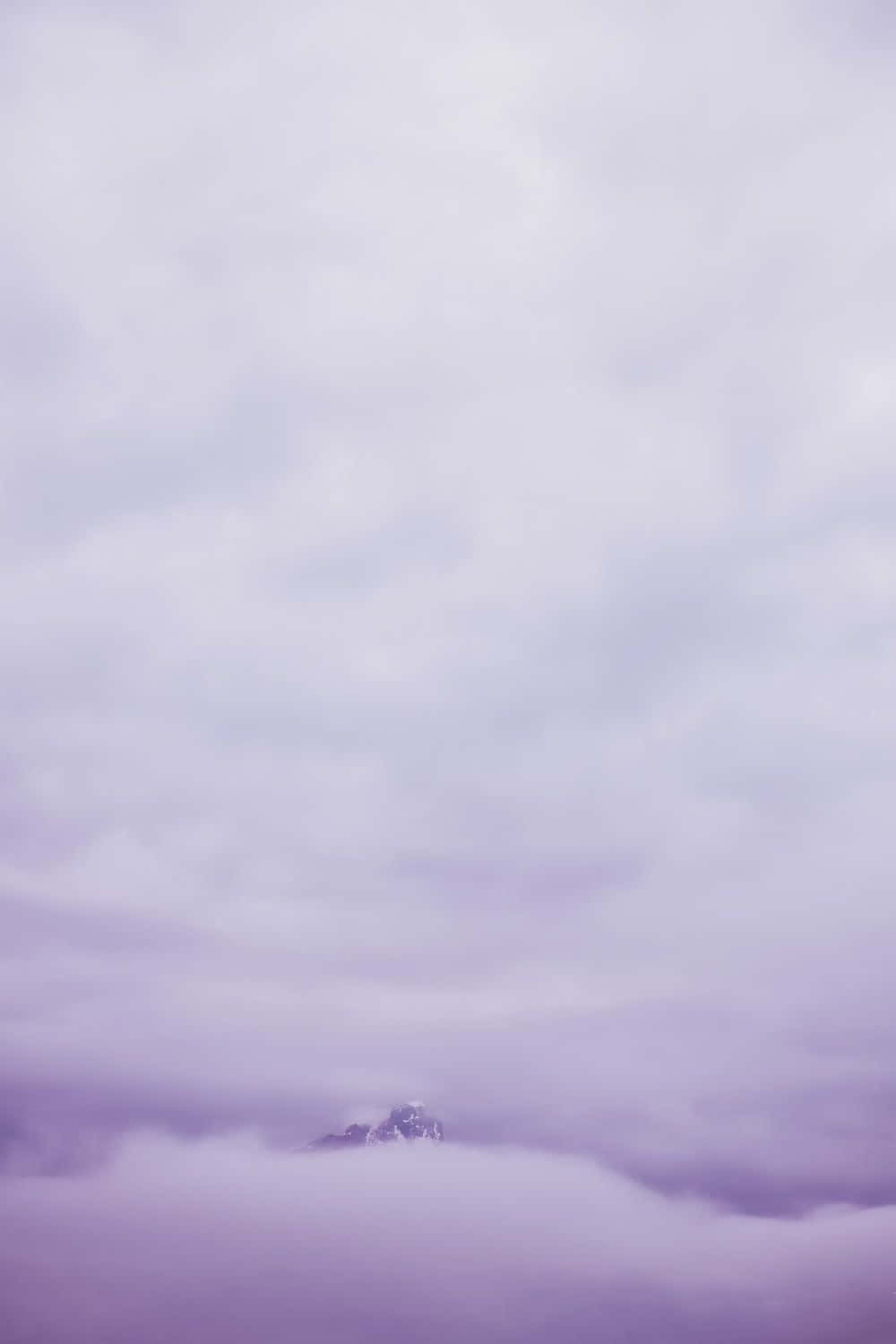 Purple Clouds 桌布 壁紙 — 一座孤獨的雪山頂峰從柔和的薰衣草色雲海中浮現，天空色調柔和。
