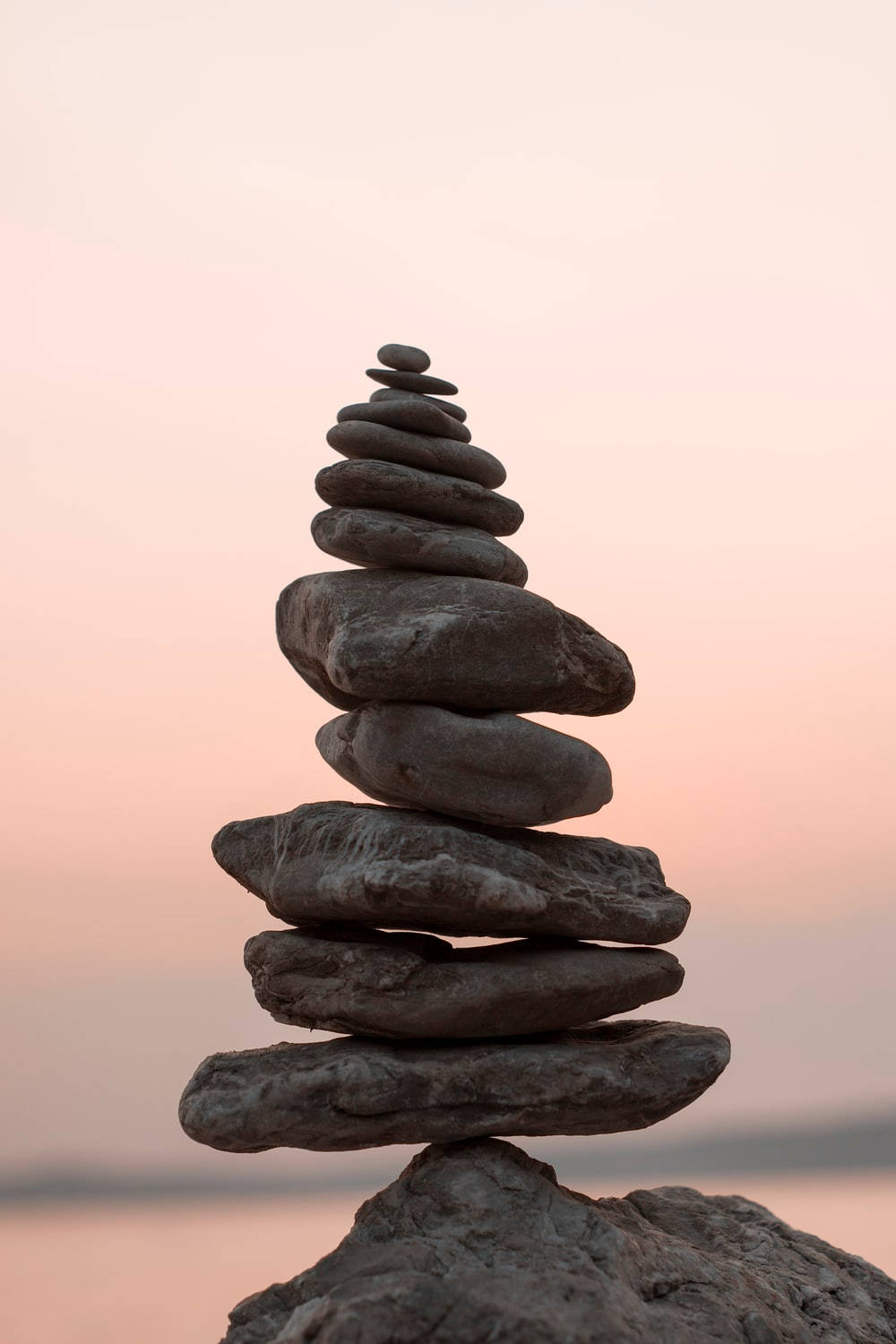 靈性動圖 桌布 壁紙 — 一座完美平衡的平滑石塔在柔和粉紅與蜜桃色的日落天空中升起。