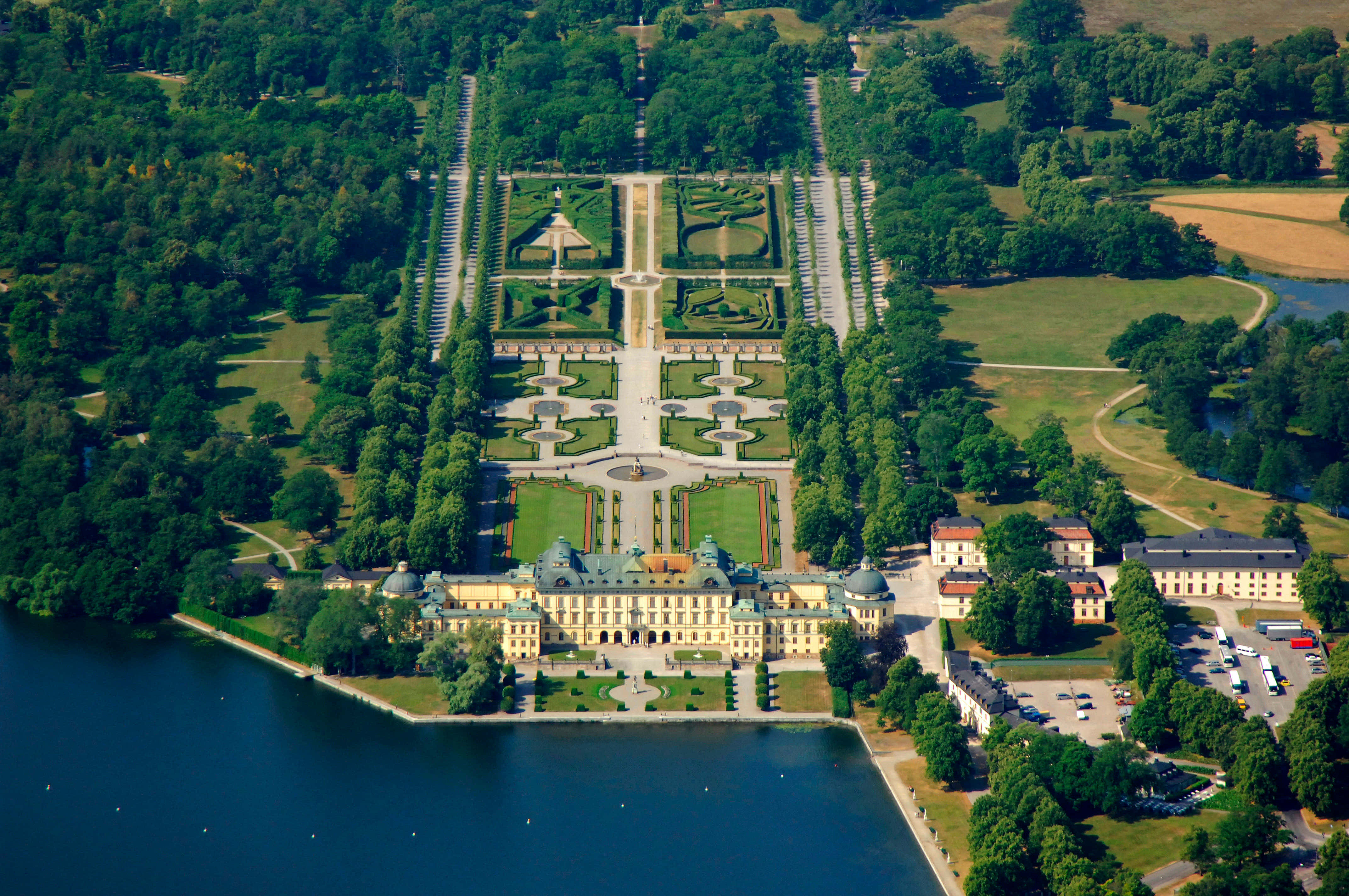 Drottningholm Palace 桌布 壁紙 — 一座宏偉巴洛克宮殿的鳥瞰圖，擁有對稱花園，兩側是茂密森林和一個大湖。