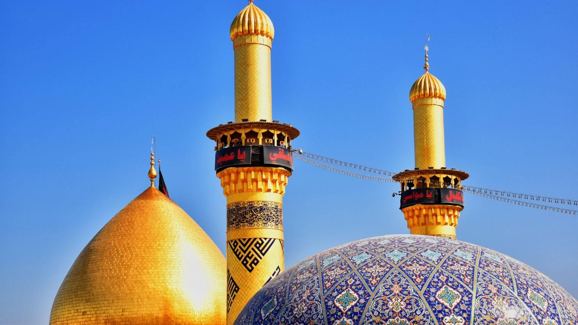 Baghdad 桌布 壁紙 — 一座宏偉清真寺的金色圓頂和宣禮塔在晴朗的藍天下閃耀，帶有精緻的瓷磚圖案。