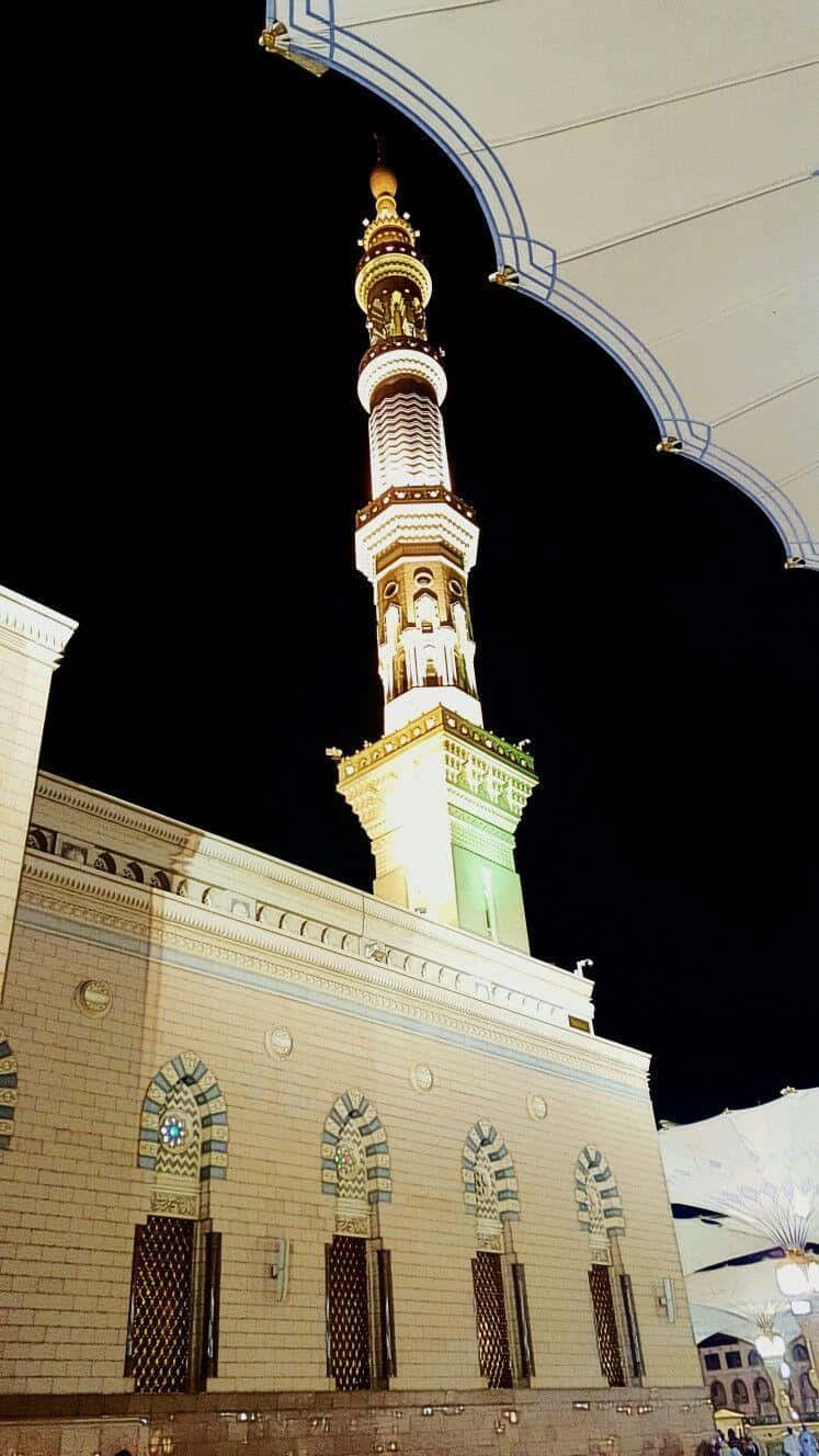 Medina 桌布 壁紙 — 一座宏偉的、被照亮的清真寺宣禮塔在黑暗的夜空中升起，由拱形建築結構框住。