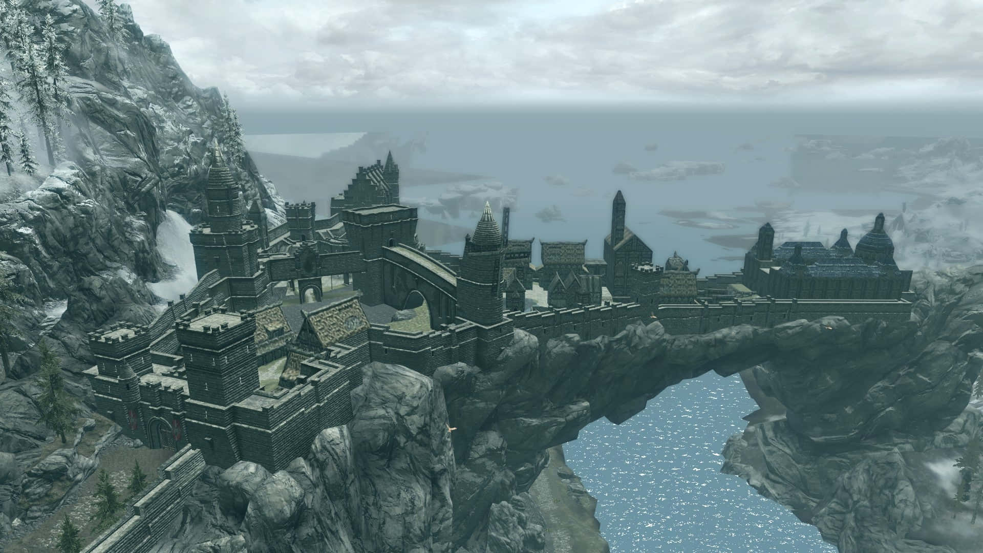 Skyrim Solitude 桌布 壁紙 — 一座宏偉的中世紀城堡坐落在懸崖上，俯瞰著廣闊的海洋，遠處是白雪皚皚的山脈。