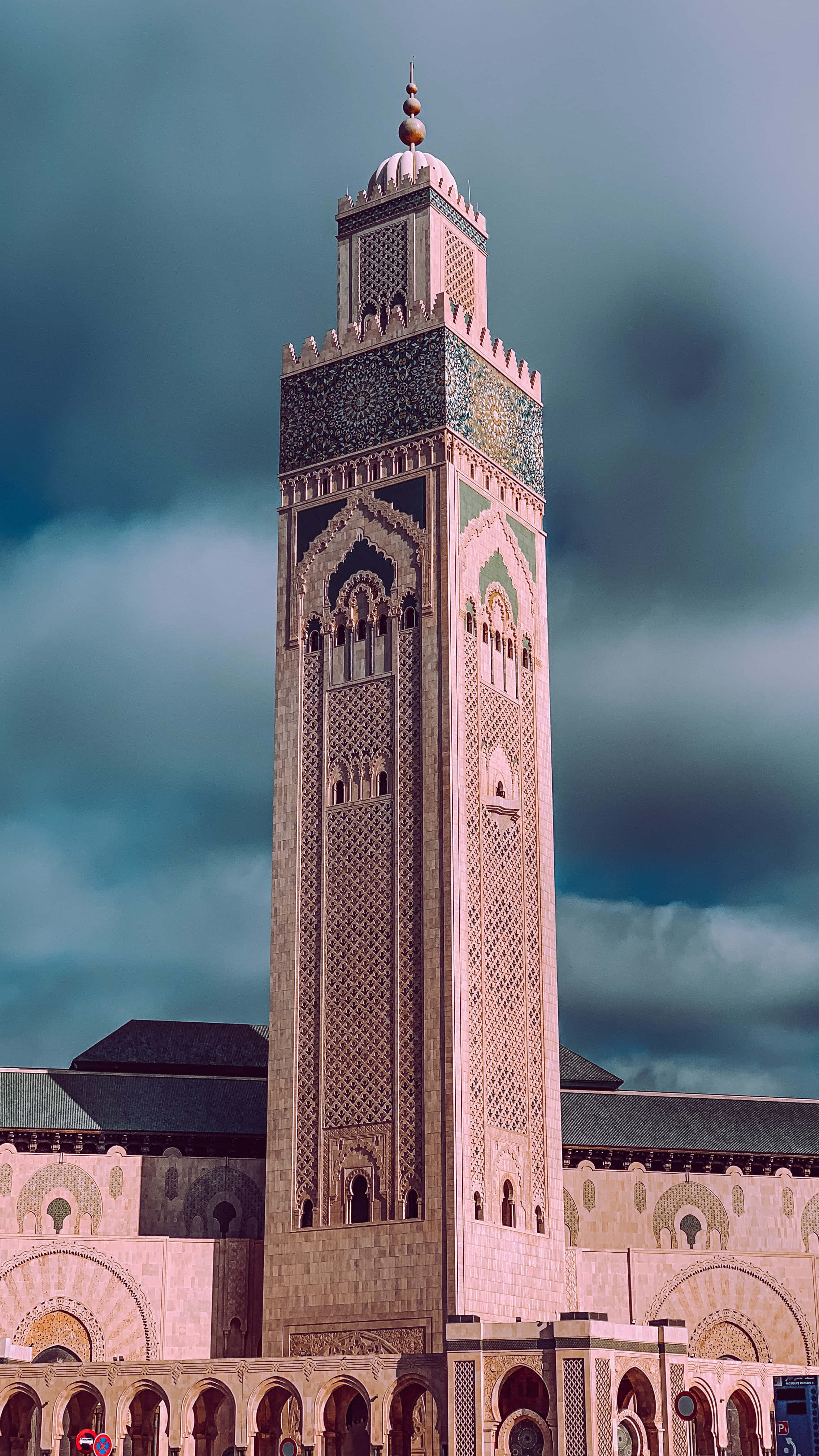 Mosque 桌布 壁紙 — 一座宏偉的伊斯蘭清真寺宣禮塔，帶有複雜的幾何圖案，聳立在戲劇性的多雲天空背景下。