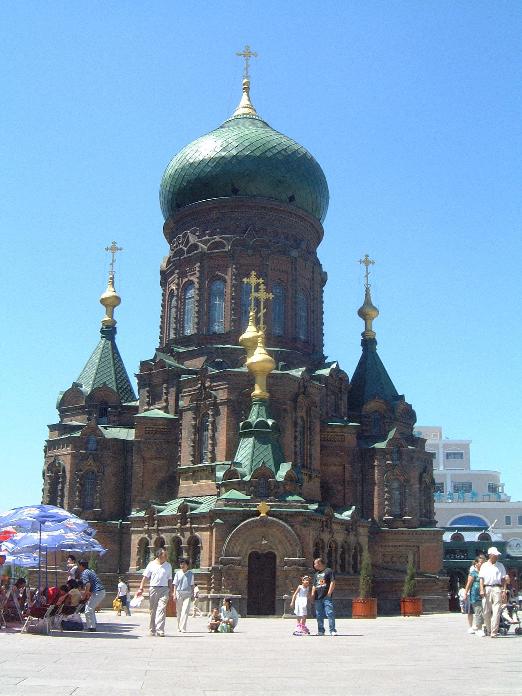 Harbin 桌布 壁紙 — 一座宏偉的俄羅斯東正教教堂，擁有綠色圓頂和金色十字架，矗立在晴朗的藍天下，人們在廣場上漫步。