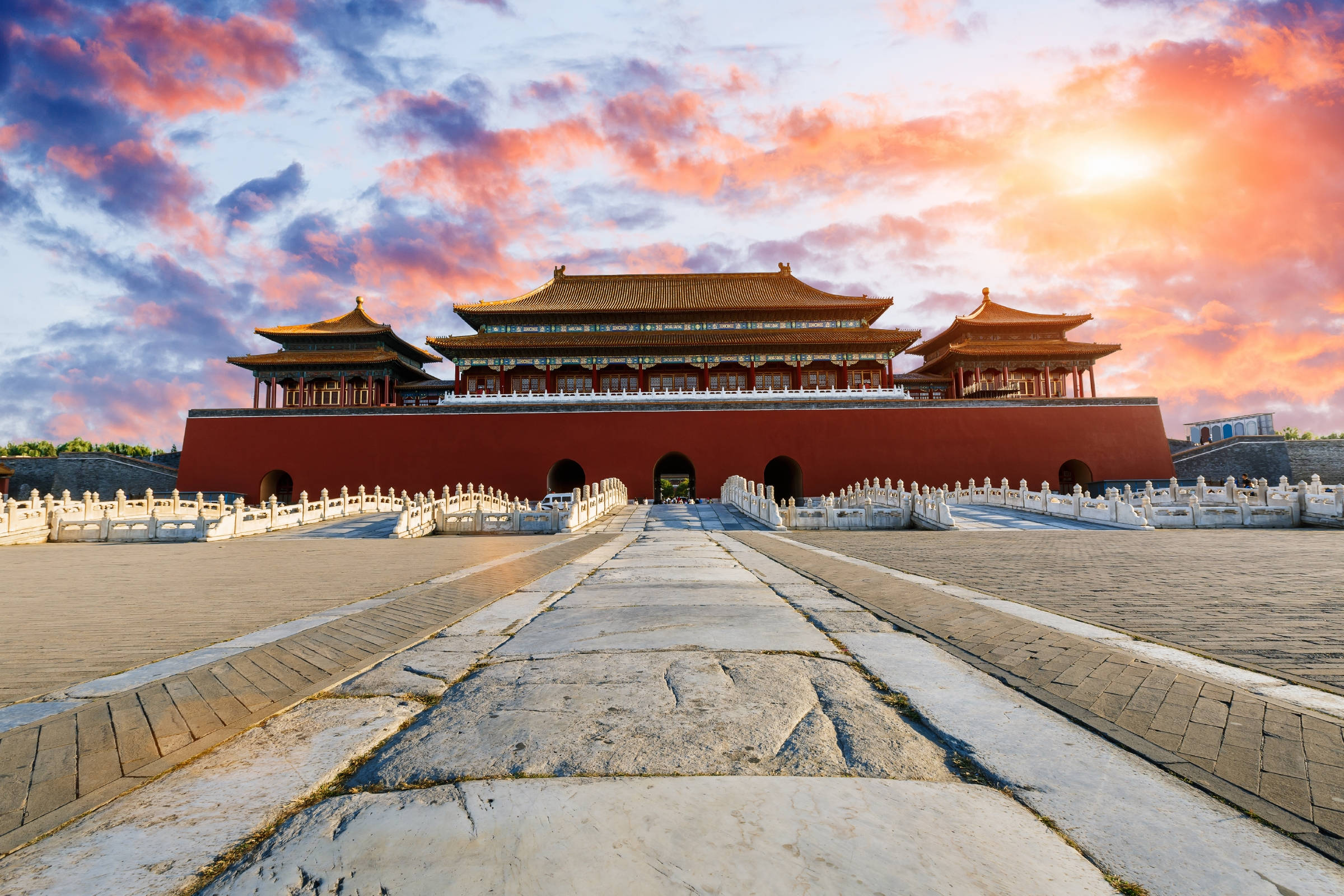 中國 桌布 壁紙 — 一座宏偉的傳統中國宮殿大門沐浴在溫暖的夕陽色調中，上方有戲劇性的粉紅色和橙色雲彩。